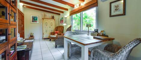 A dining area with a wooden table and wicker chairs, a cabinet with glass doors, and a window with a view of greenery.