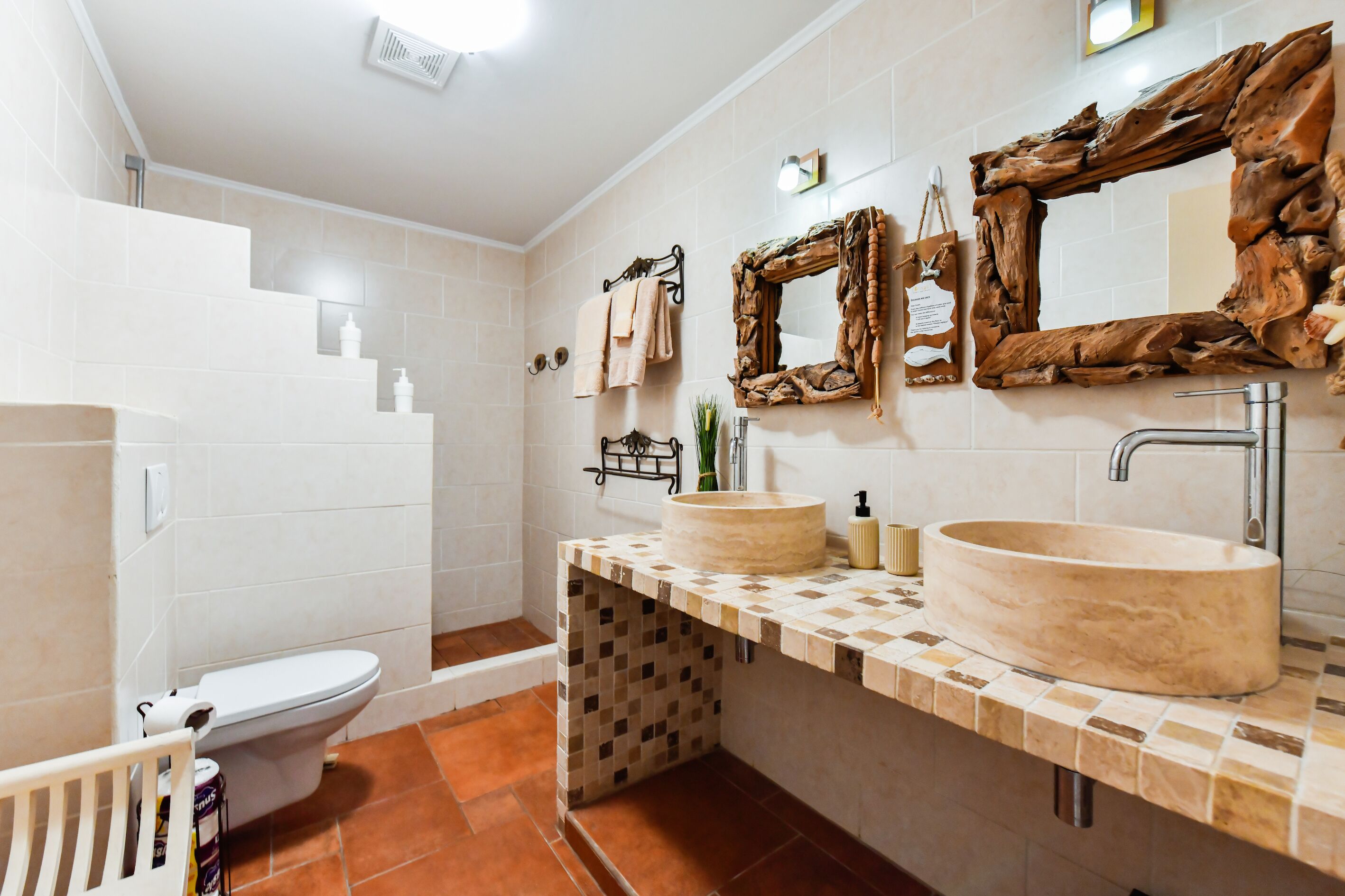 Une salle de bain avec des toilettes blanches, un lavabo doté d’un plan de travail en bois et un miroir avec un cadre en bois.
