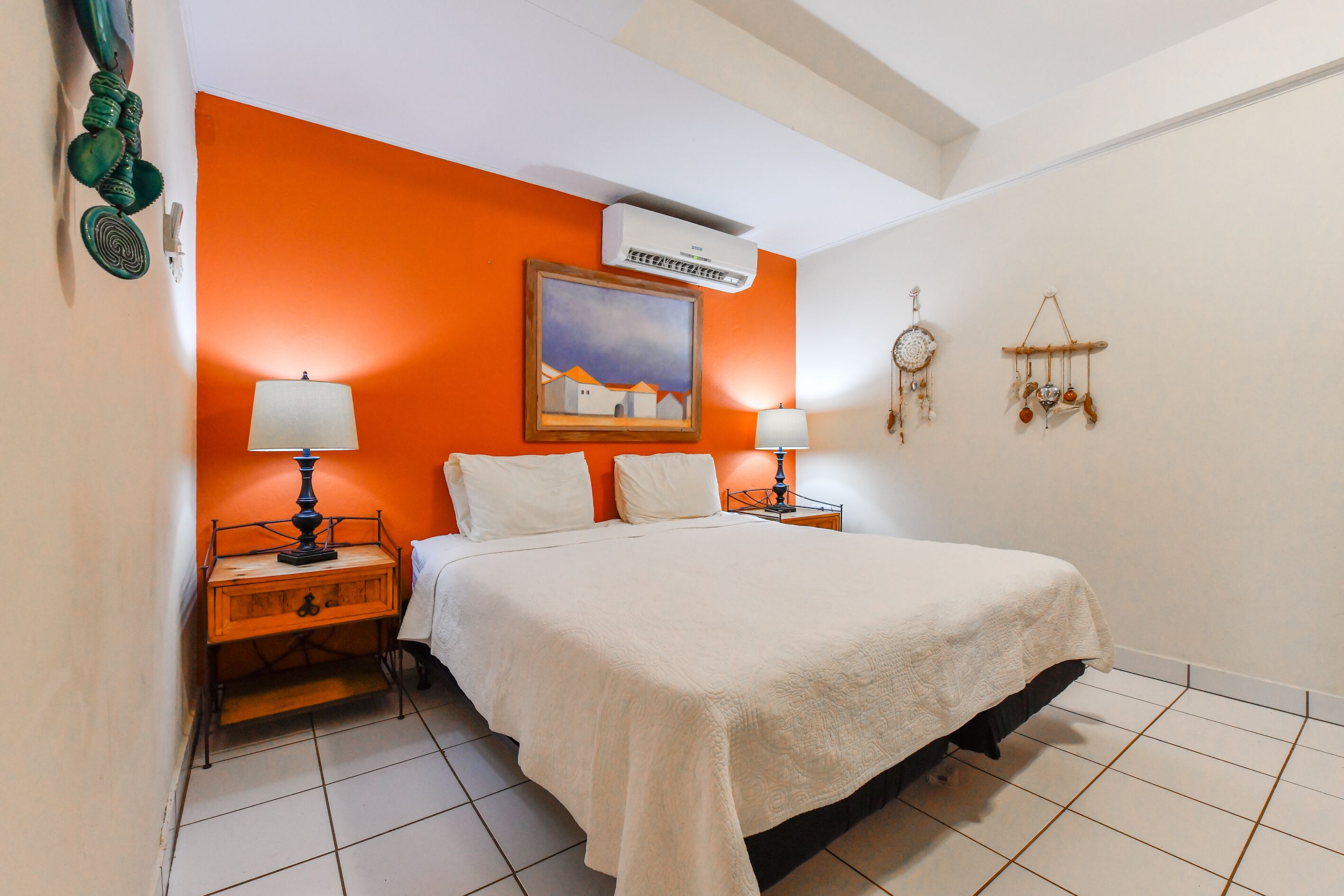 Een slaapkamer met een bed, twee nachtkastjes, een airconditioner, een schilderij en wanddecoraties.