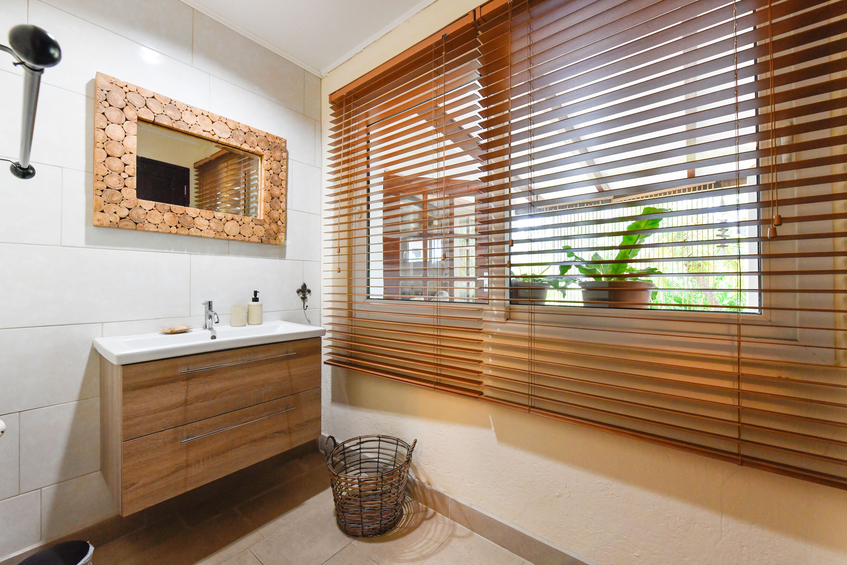 A bathroom with a wooden vanity, a mirror with a wooden frame, and a window with blinds.