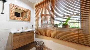 A bathroom with a wooden vanity, a mirror with a wooden frame, and a window with blinds.