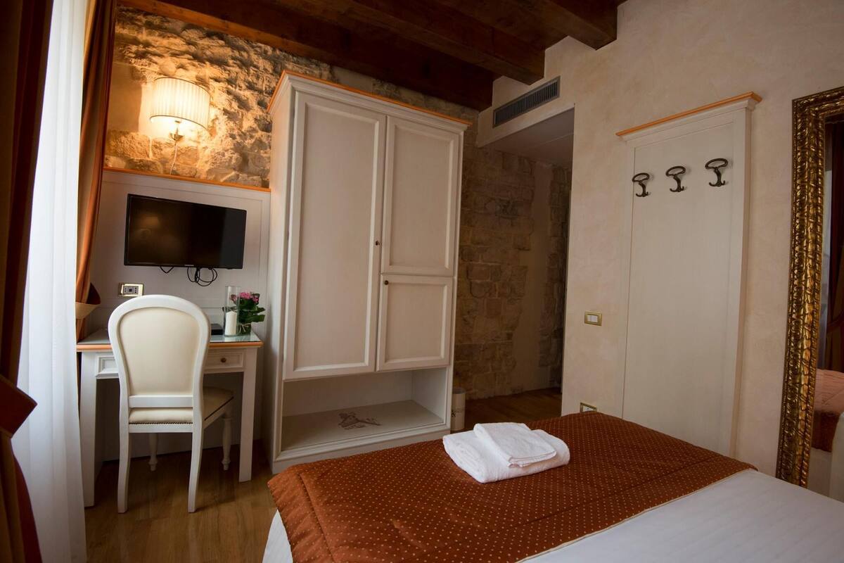 A bedroom with a bed, a desk, a chair, a wardrobe, and a television.
