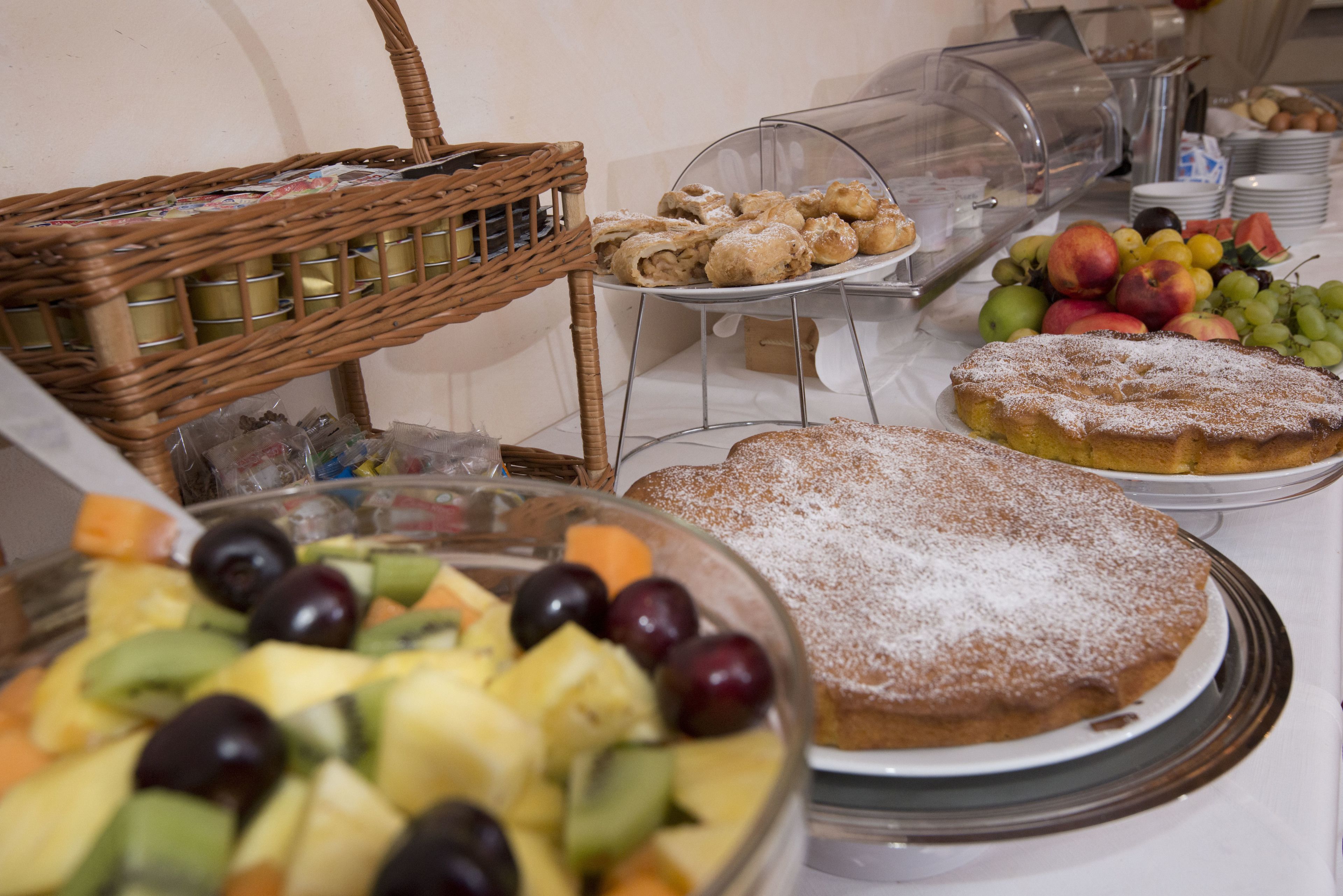 A buffet with various food items including fruits, pastries, and a covered display case.