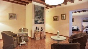 Amplia habitación con techo alto, vigas de madera y un cuadro grande de un paisaje urbano. Varias sillas y mesas, algunas con botellas de vino y copas.