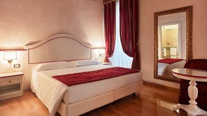 Una habitación de hotel con una cama grande, una mesita de noche con lámpara, un espejo y una pequeña mesa redonda.