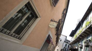 A narrow street with buildings featuring traditional architecture, including a sign for 'Albergo Mazzani' and a visible entrance to a shop.