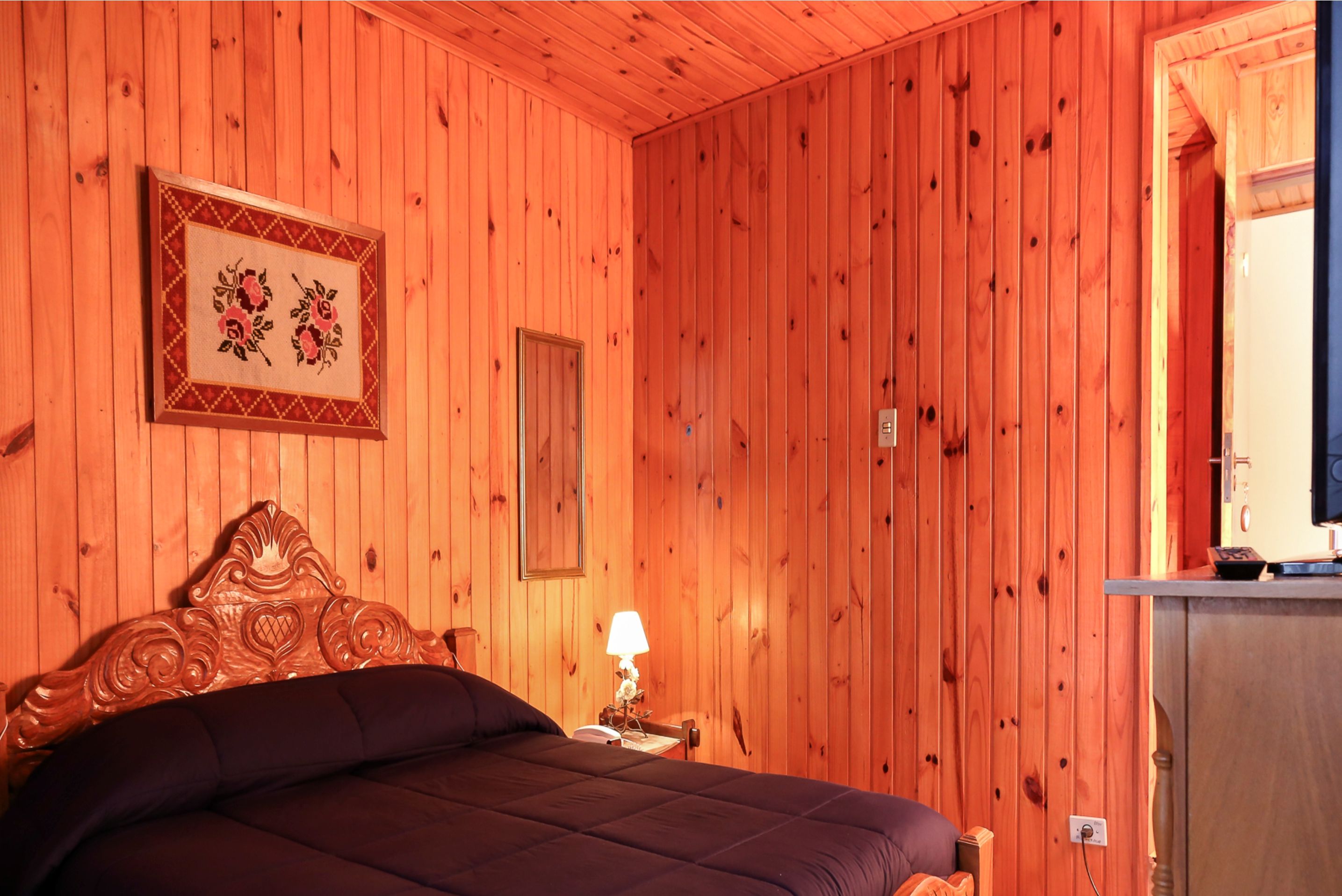 A wooden-paneled room with a bed, a nightstand, and a framed picture on the wall.