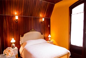 A bedroom with a wooden ceiling, a bed with a white headboard, two bedside lamps, and a nightstand with a floral arrangement. - Pousada Vale Verde (Campos do Jordão)