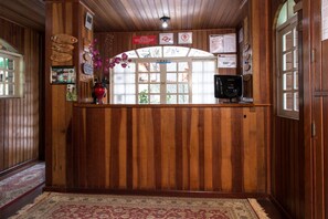 A wooden reception desk with a vase of flowers, framed pictures, and informational signs. - Pousada Vale Verde (Campos do Jordão)