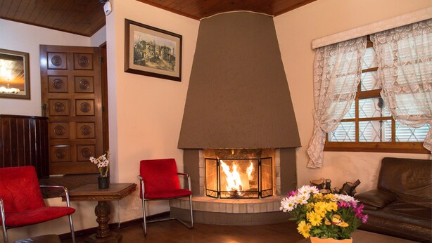 Una sala de estar acogedora con chimenea, sillones rojos, un sofá de cuero marrón y una mesa de centro de madera con un jarrón de flores.