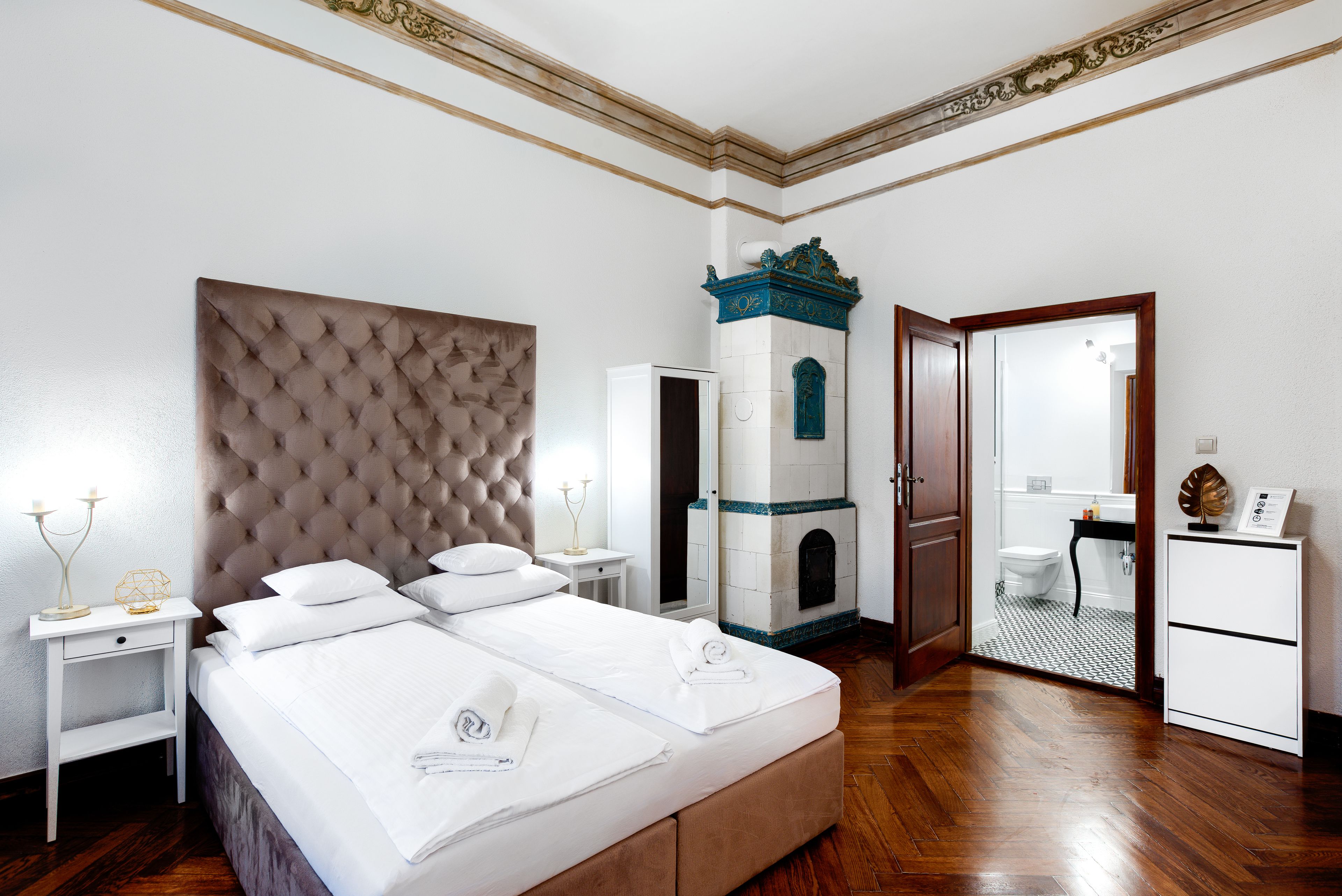 Quarto de hotel com cama grande, mesa de cabeceira, cômoda, banheiro e teto decorativo.