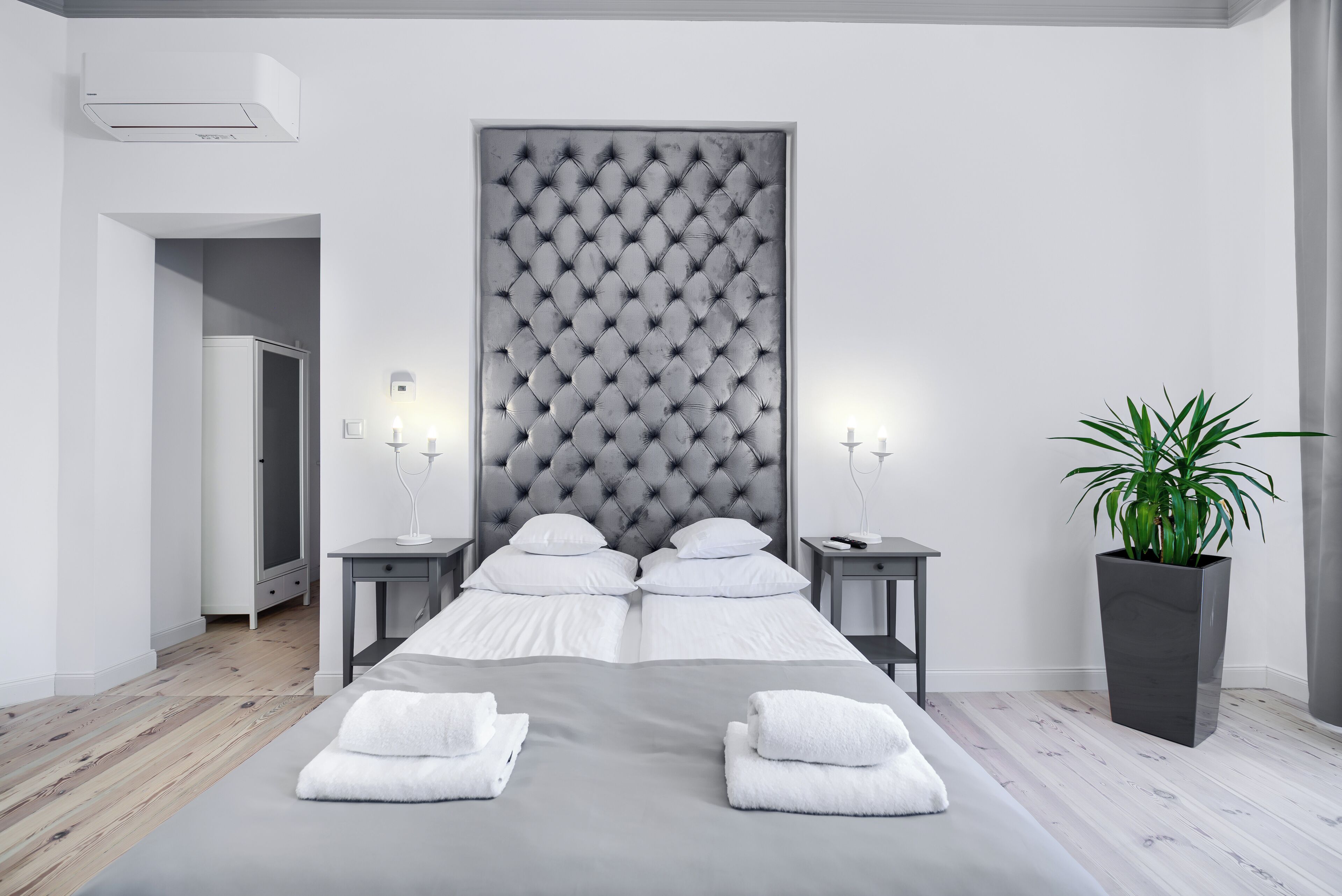 A modern hotel room with a large bed, two bedside tables, a potted plant, and a grey headboard.