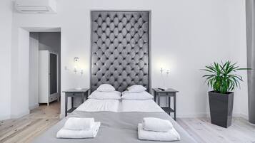 Ein modernes Hotelzimmer mit einem großen Bett, zwei Nachttischen, einer Topfpflanze und einem grauen Kopfteil.
