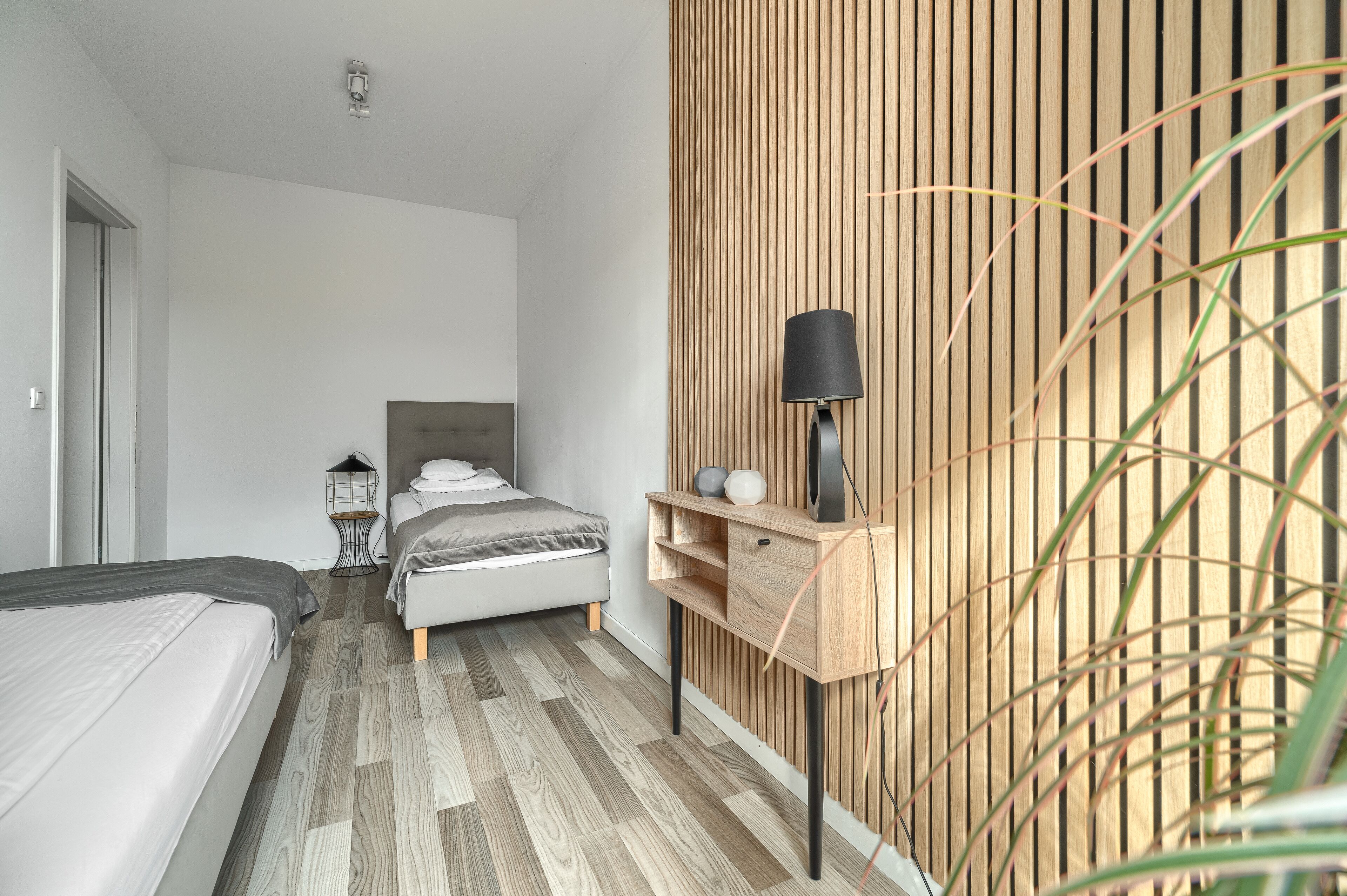 A modern bedroom with a bed, bedside table, lamp, and a wooden wall panel.