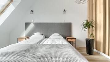 A modern bedroom with a large bed, two bedside tables, a potted plant, and a sloped ceiling with skylight.