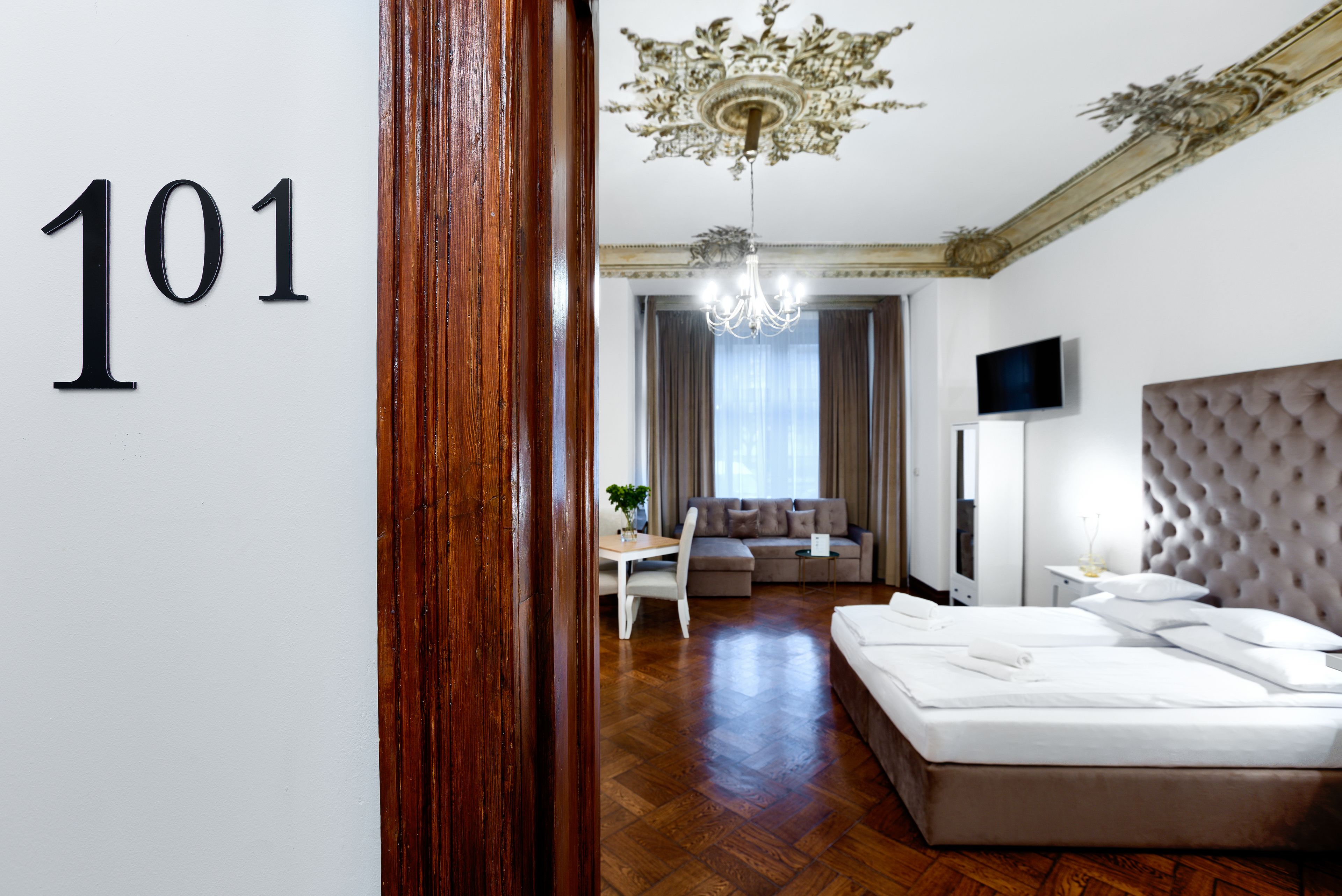 Hotellihuone, jossa on suuri sänky, sohva, televisio ja kattokruunu.