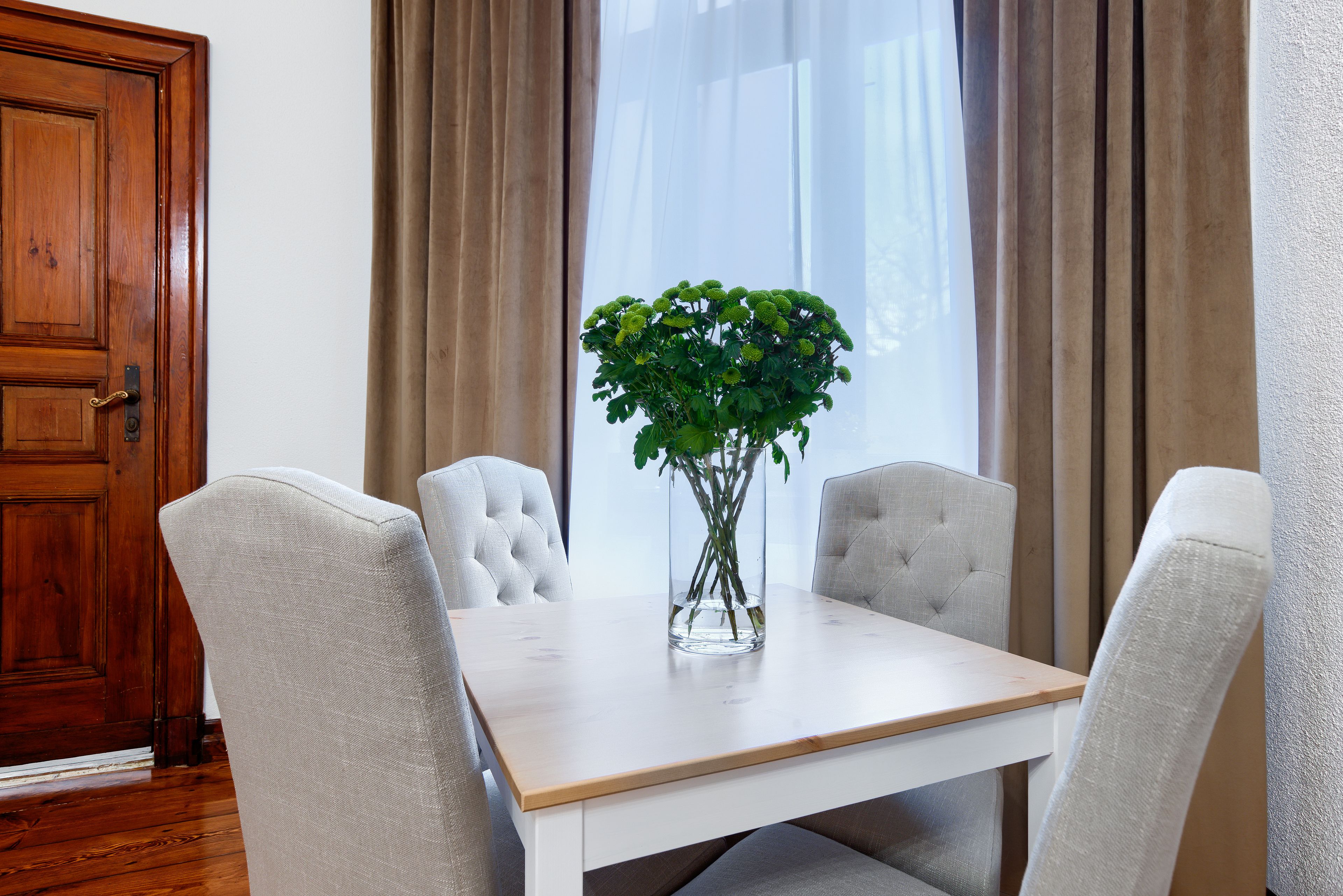A dining table with four upholstered chairs, a vase with green plants, and a wooden door.