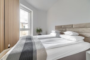 A modern bedroom with a large bed, a wooden slat wall, and a view of the outside.