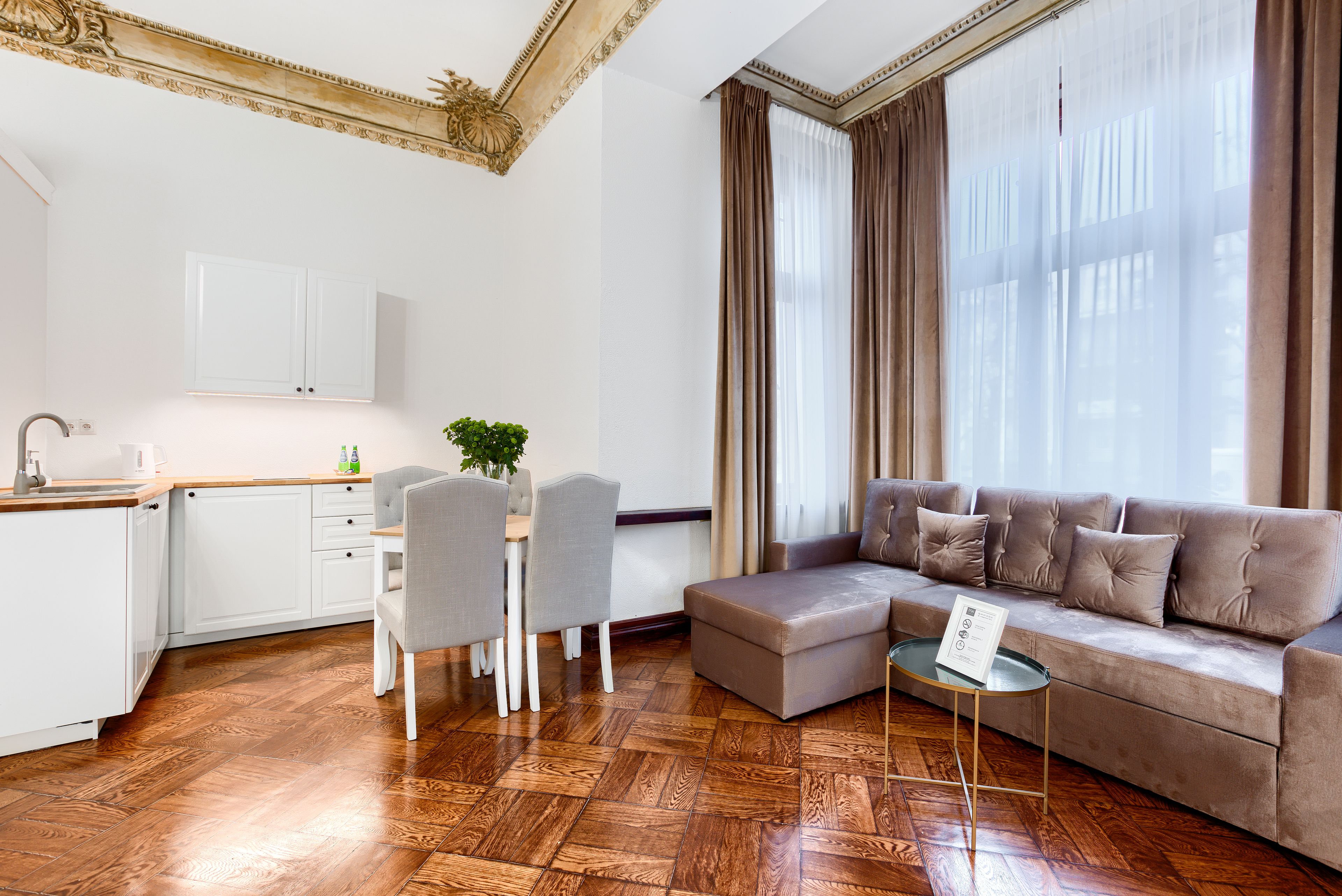 A modern living room with a sofa, a dining table with chairs, and a kitchen area with cabinets and a countertop.