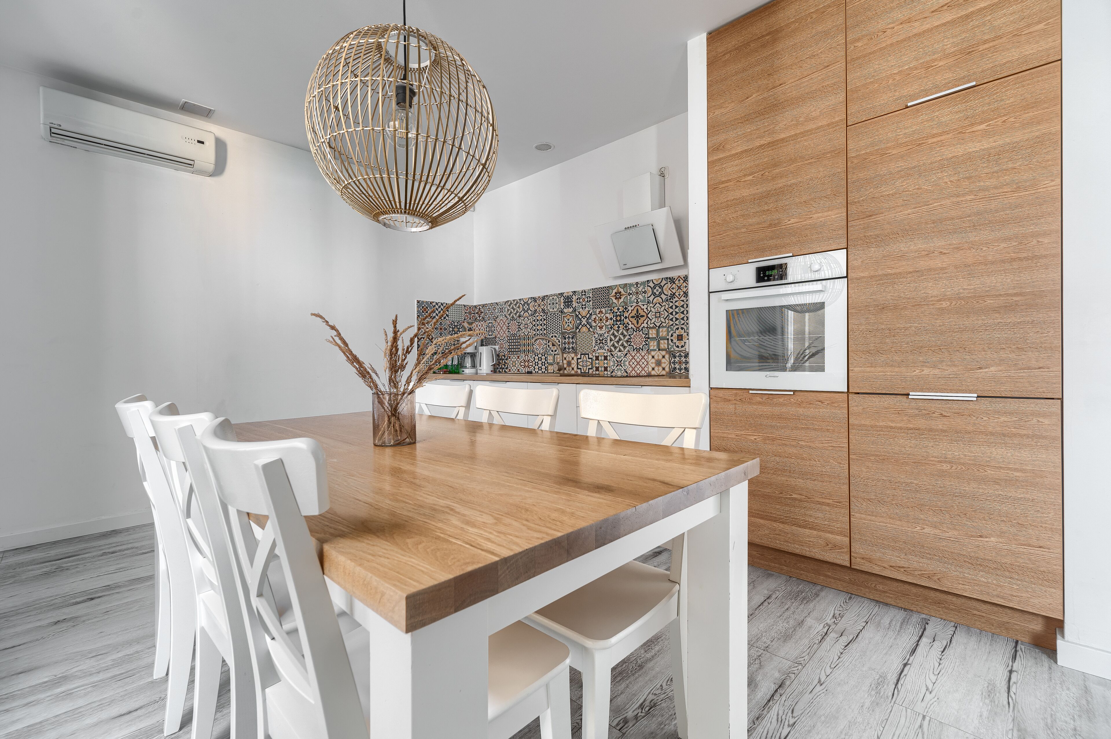 Eine moderne Küche mit einem Holztisch, weißen Stühlen, einer gemusterten Spritzschutzwand und Holzschränken.