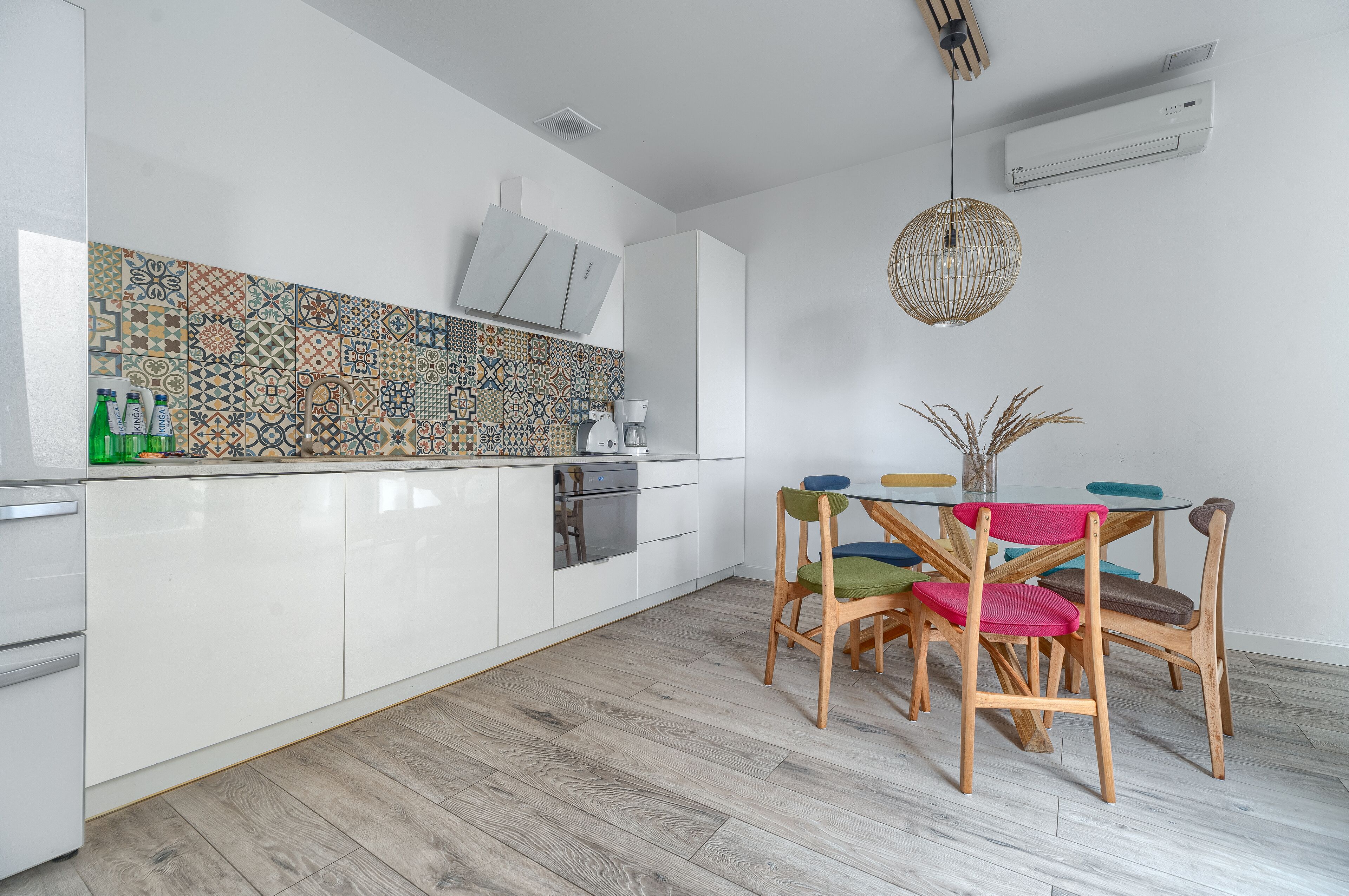 A modern kitchen with white cabinets, a patterned backsplash, and a dining area with wooden chairs and a table.