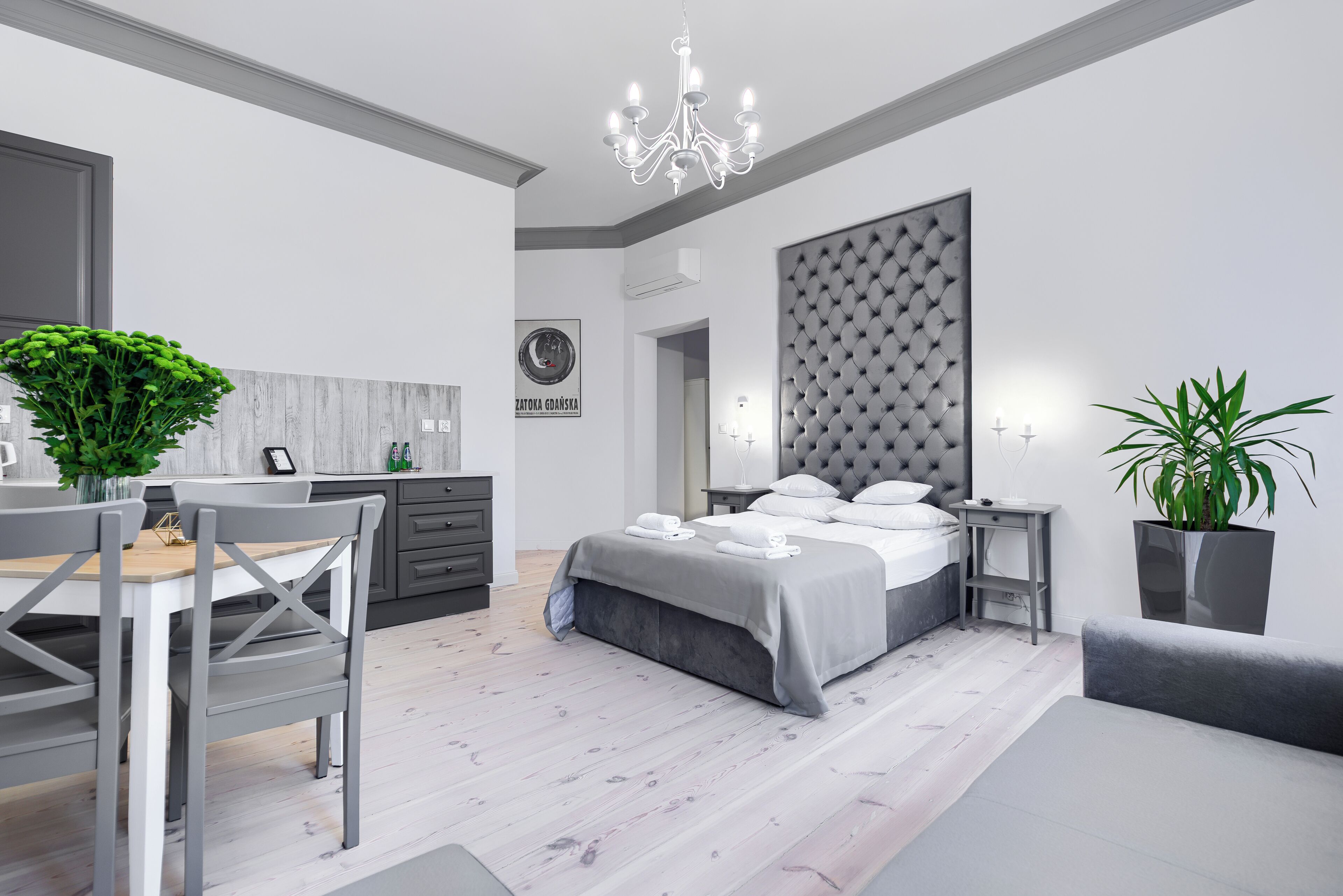 Een moderne slaapkamer met een bed, nachtkastjes, een kroonluchter en een zithoek met stoelen en een tafel.
