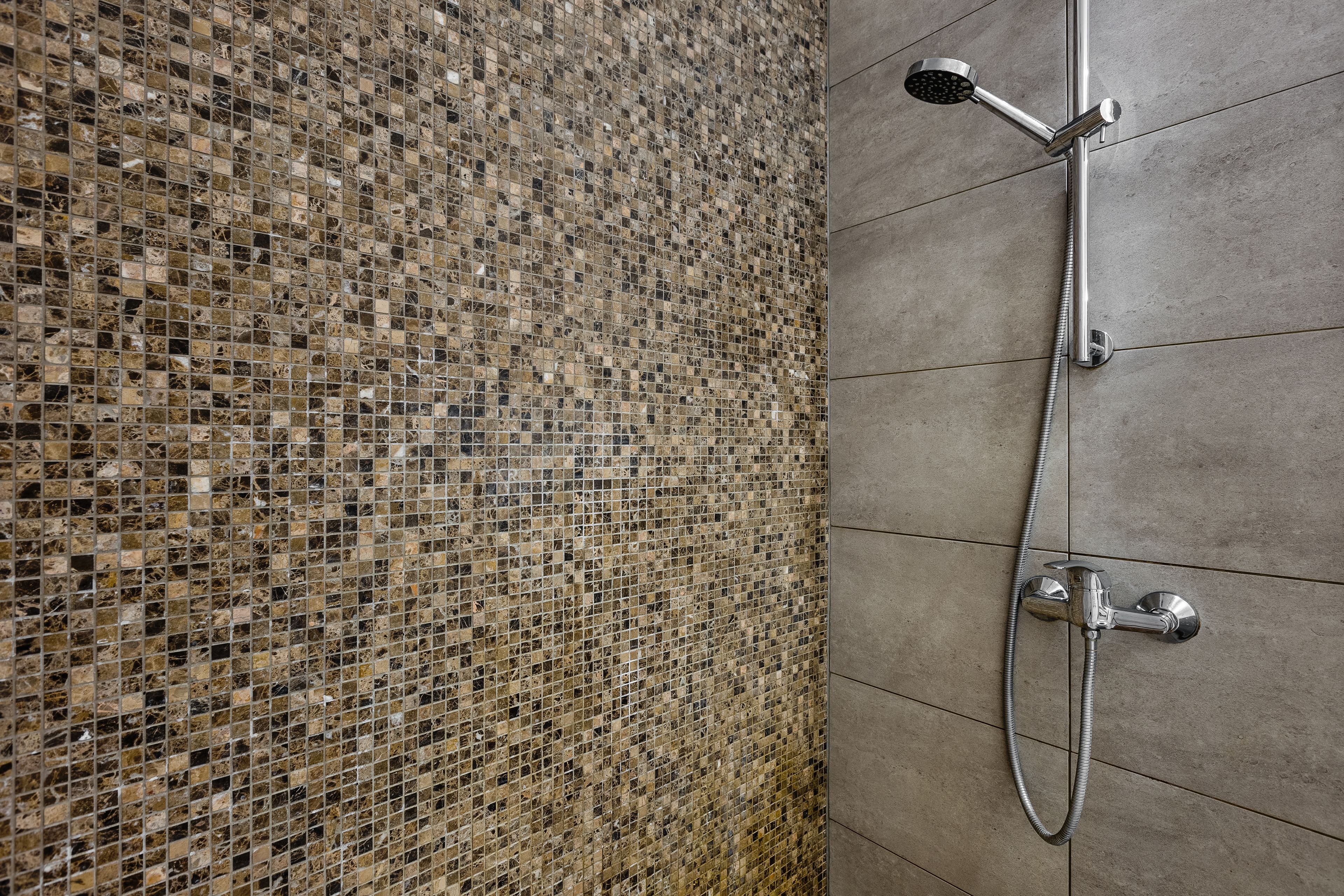Un espace douche avec un mur recouvert de mosaïques et une pomme de douche en chrome.