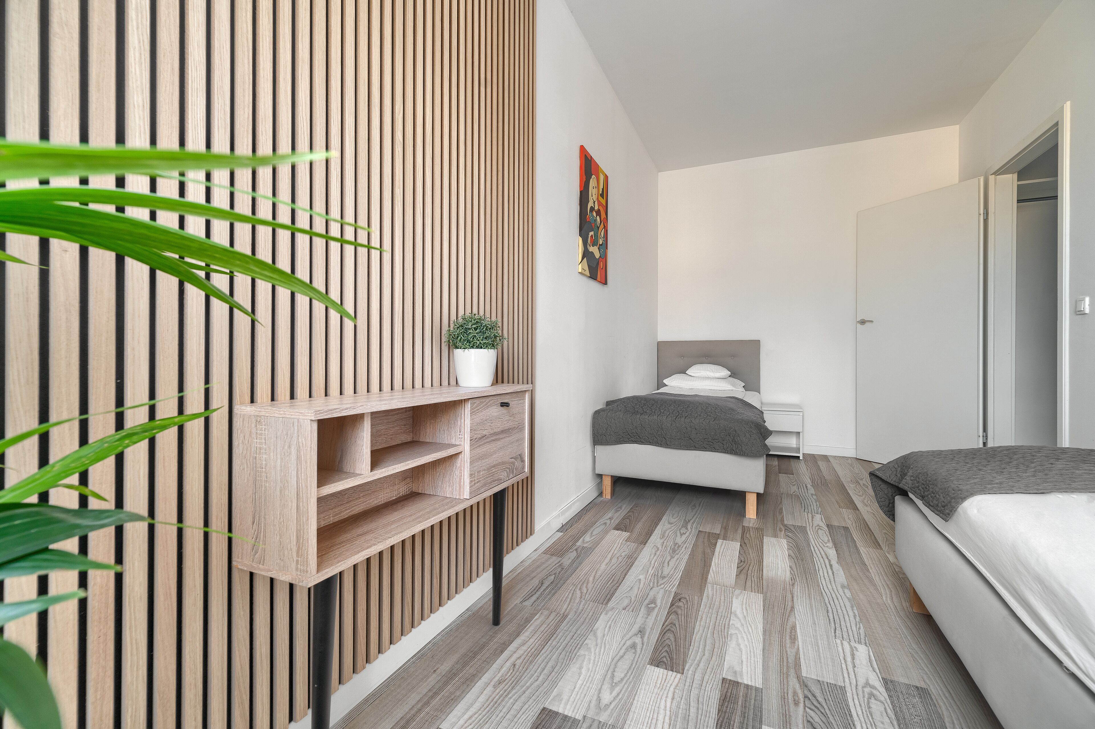 A modern bedroom with a wooden slat wall, a bed, a bedside table, and a small potted plant.