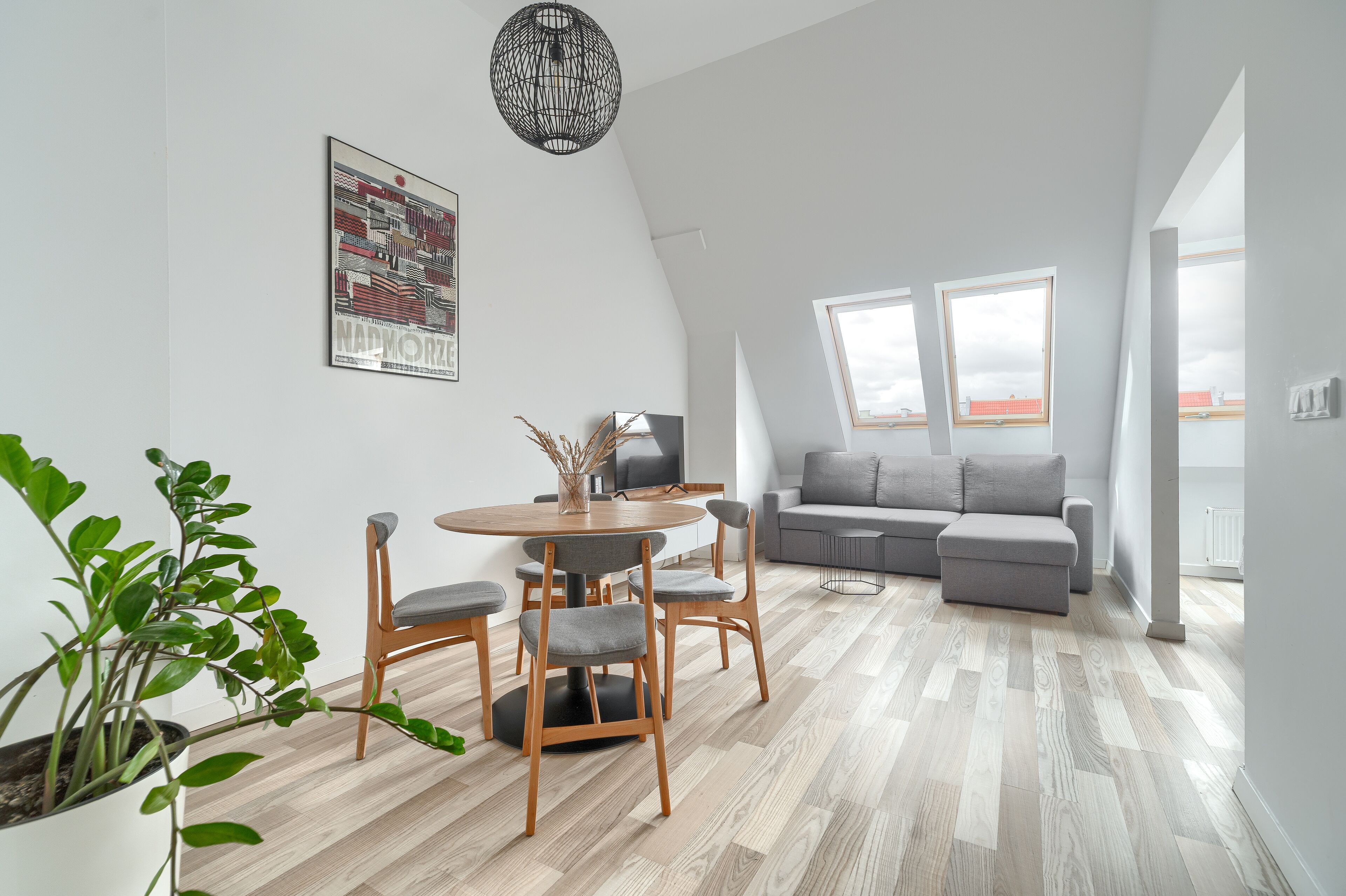 Ein modernes Wohnzimmer mit Essbereich, grauem Sofa und einem großen Fenster.
