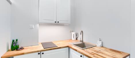 A kitchen with white cabinets, a wooden countertop, a sink, a kettle, and two green bottles.