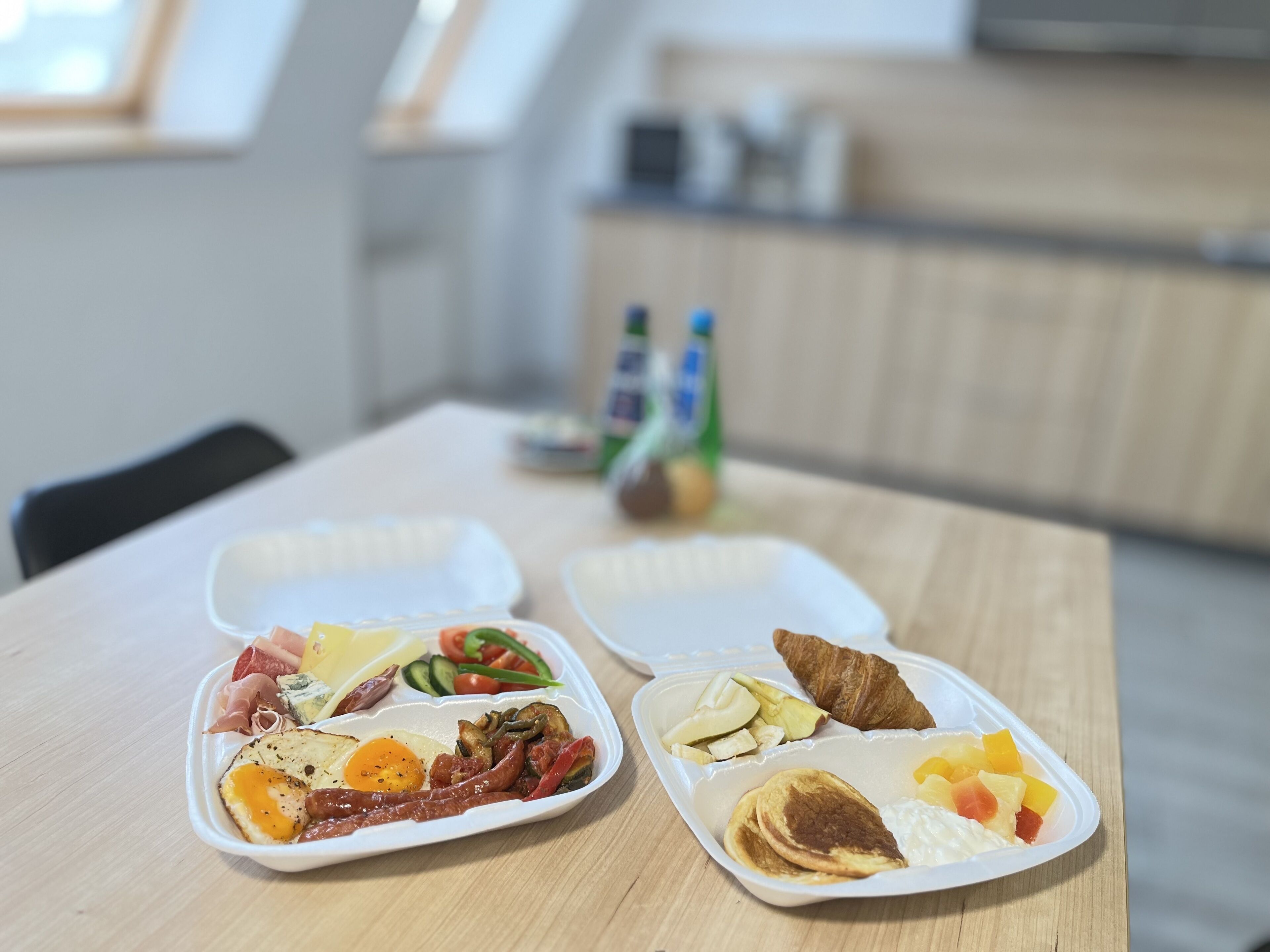 Dos recipientes de comida sobre una mesa de madera en una habitación con cocina al fondo.