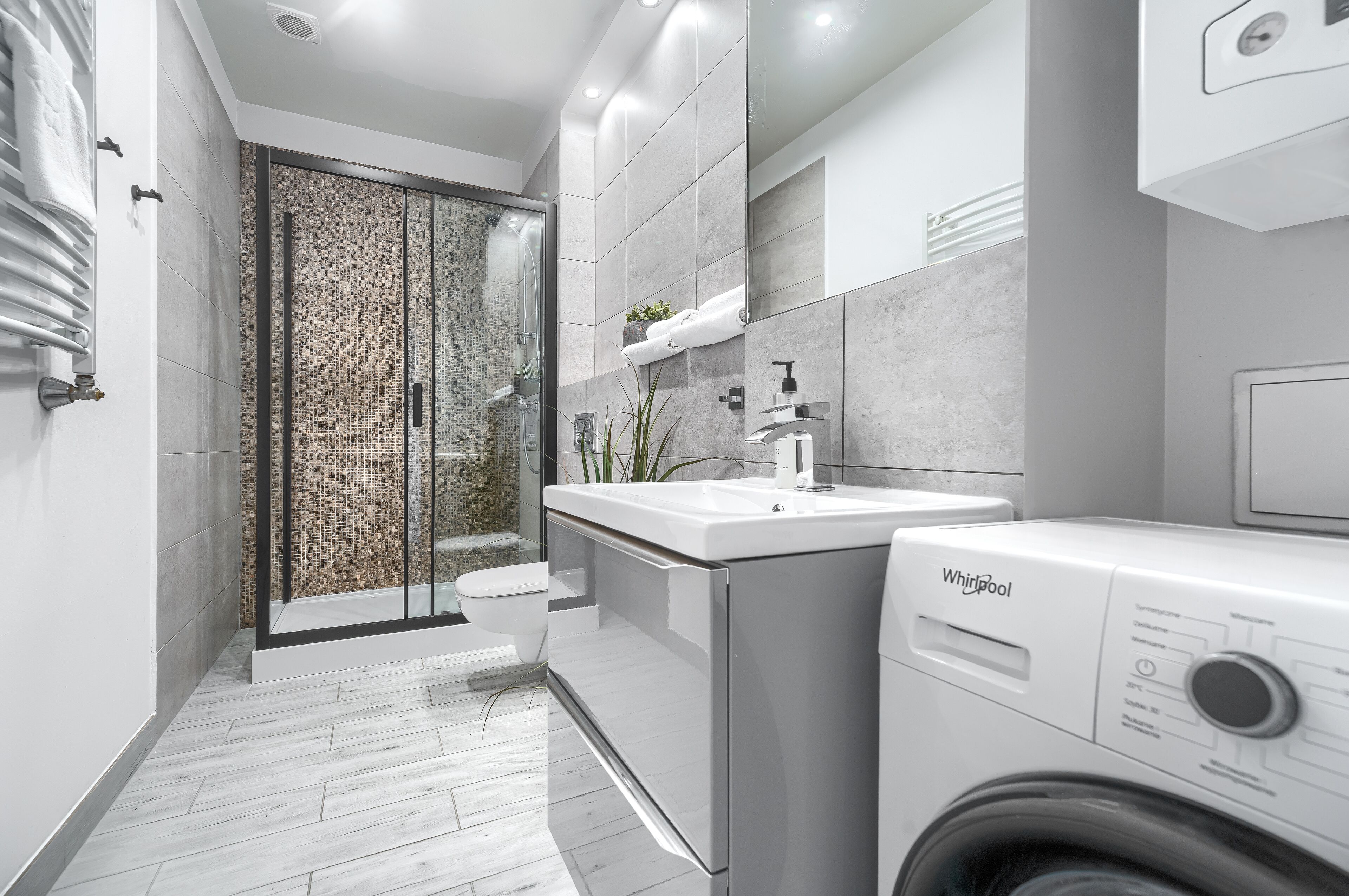 Une salle de bain moderne dotée d’une cabine de douche en verre, d’un lavabo intégré et d’un lave-linge Whirlpool.
