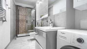 Une salle de bain moderne dotée d’une cabine de douche en verre, d’un lavabo intégré et d’un lave-linge Whirlpool.