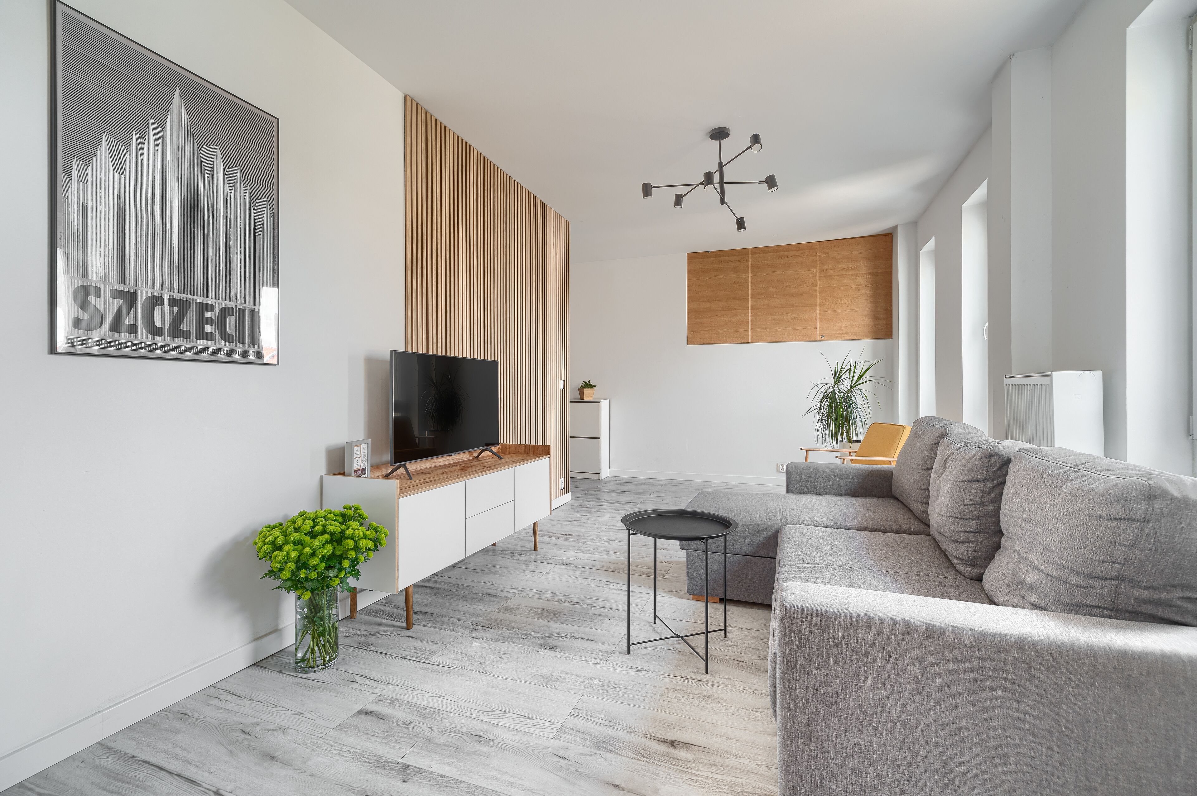 A modern living room with a TV, wooden panel wall, grey sofa, and a small table.