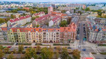 Eine Stadtansicht mit einer Mischung aus Wohn- und Geschäftsgebäuden, einem markanten Kreuzungspunkt und einem Gewässer im Hintergrund.