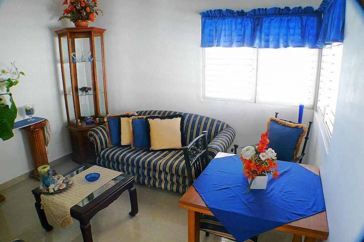 Ein Wohnzimmer mit einem gestreiften Sofa, einem Holztisch, einem Spiegel und einem Fenster mit blauen Vorhängen.