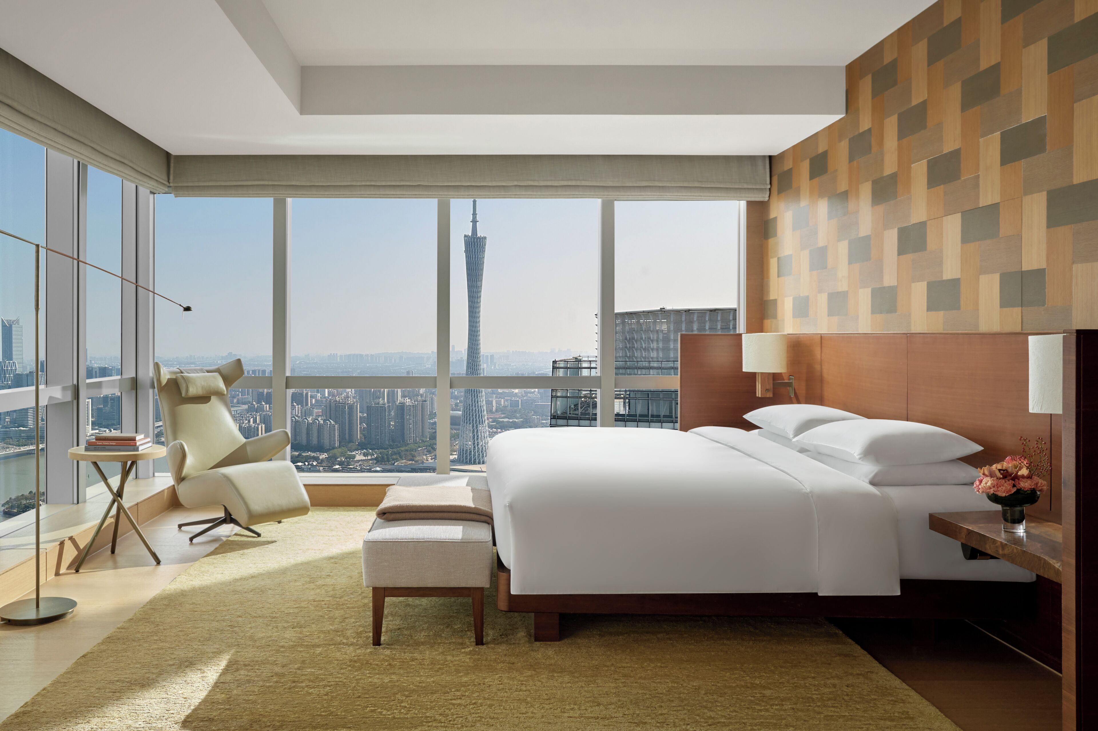 A modern hotel room with a large bed, a sitting area, and a city view.