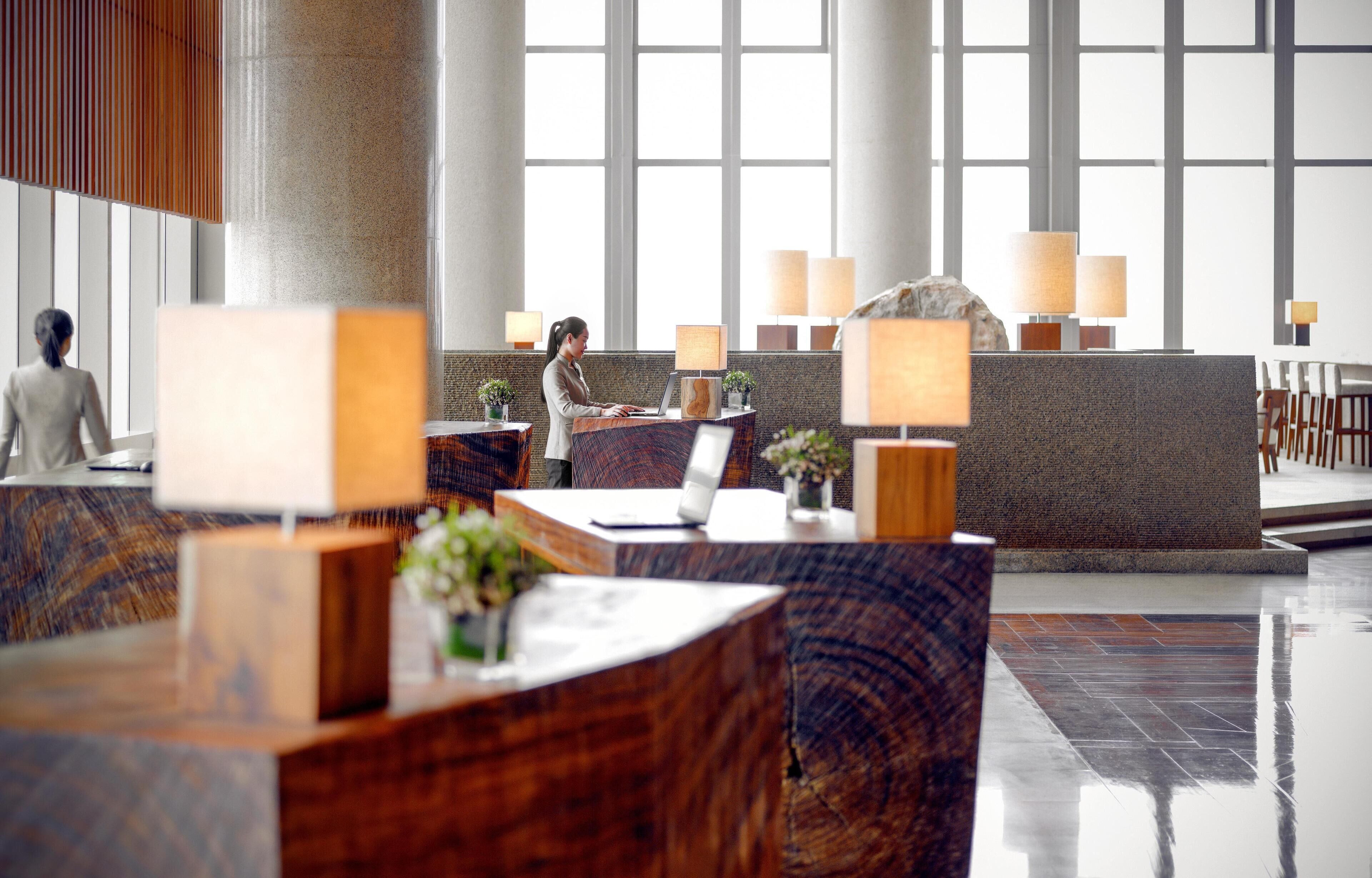 A modern hotel lobby with a reception desk, seating areas, and large windows.