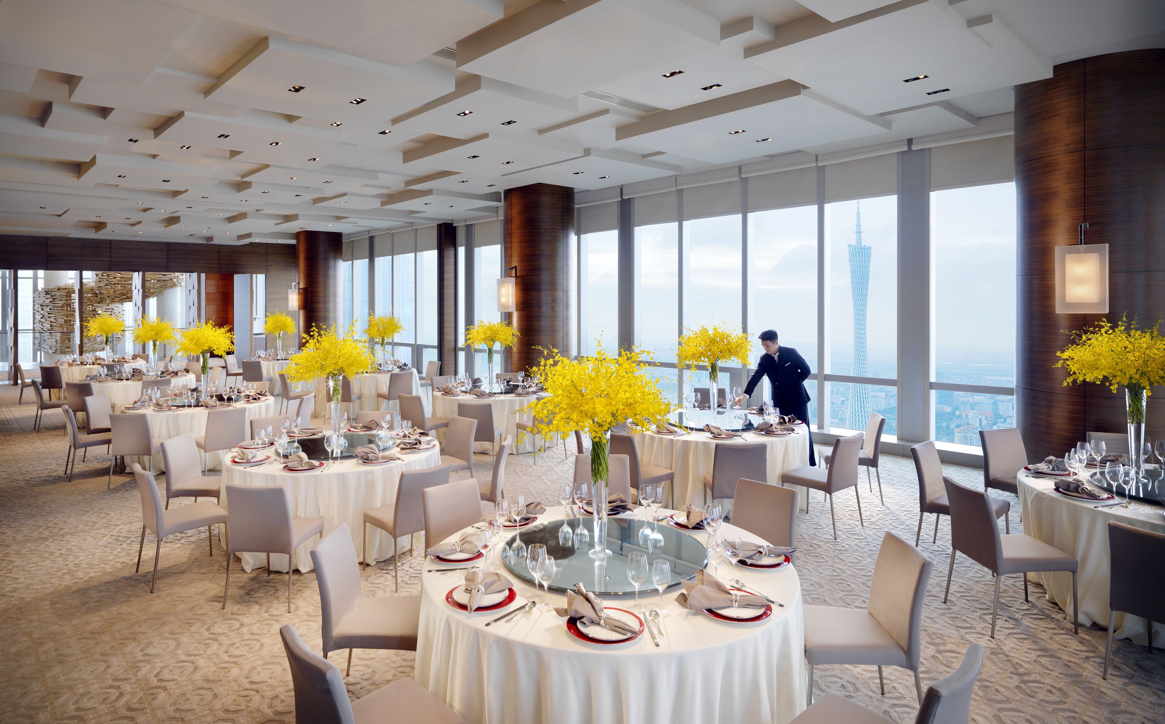 A spacious dining area with round tables, yellow flowers, and a view of a tower.