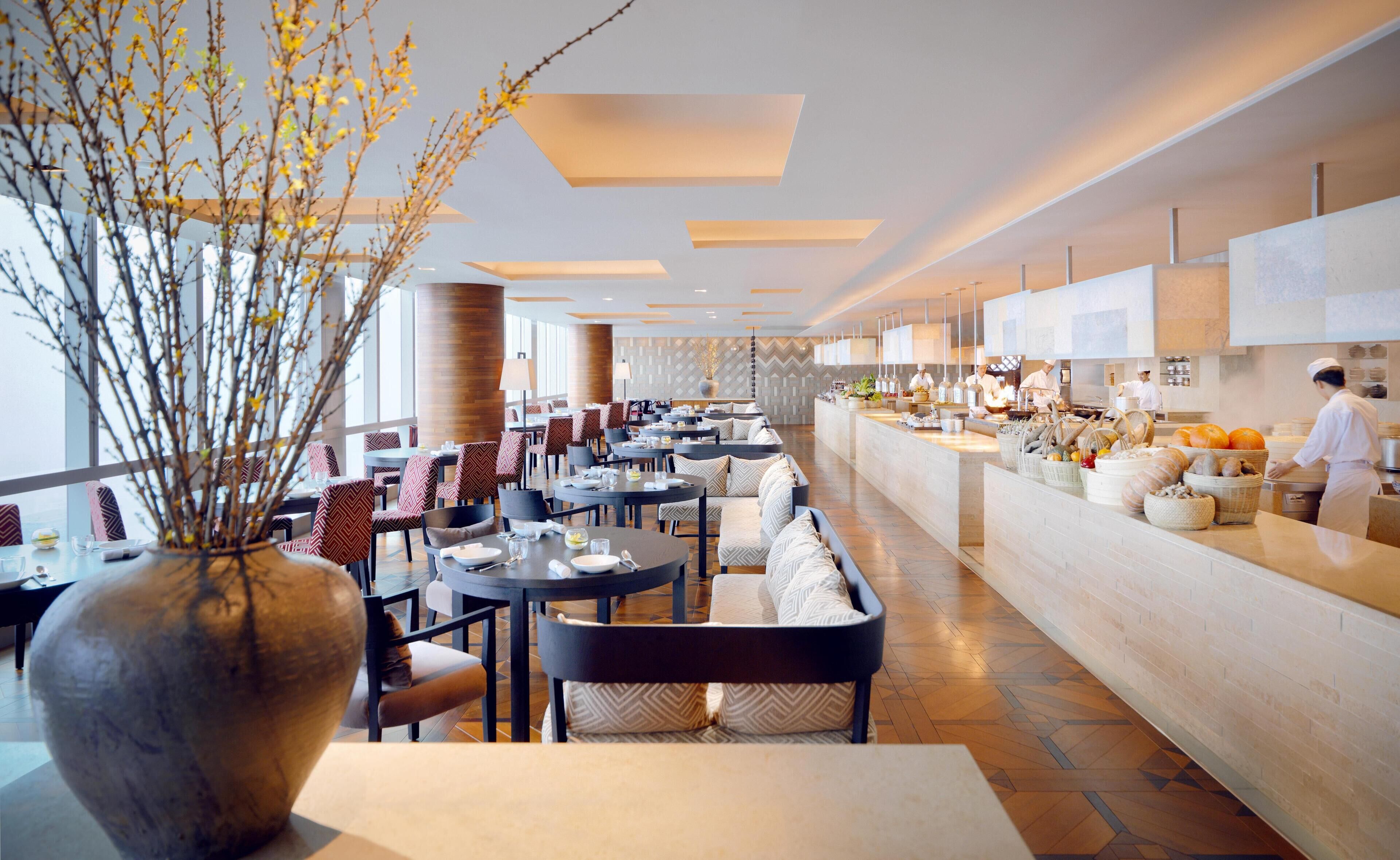 A modern restaurant with a long counter, seating area, and a decorative vase with branches.