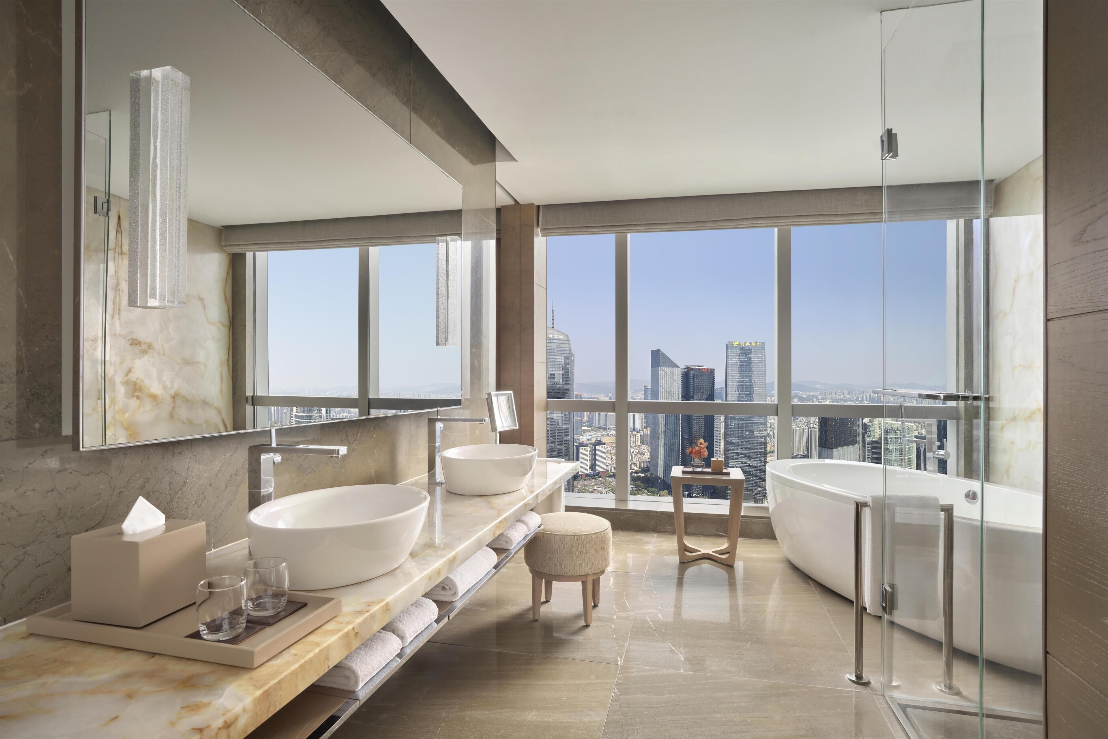 A modern bathroom with a large window, a bathtub, and two sinks.