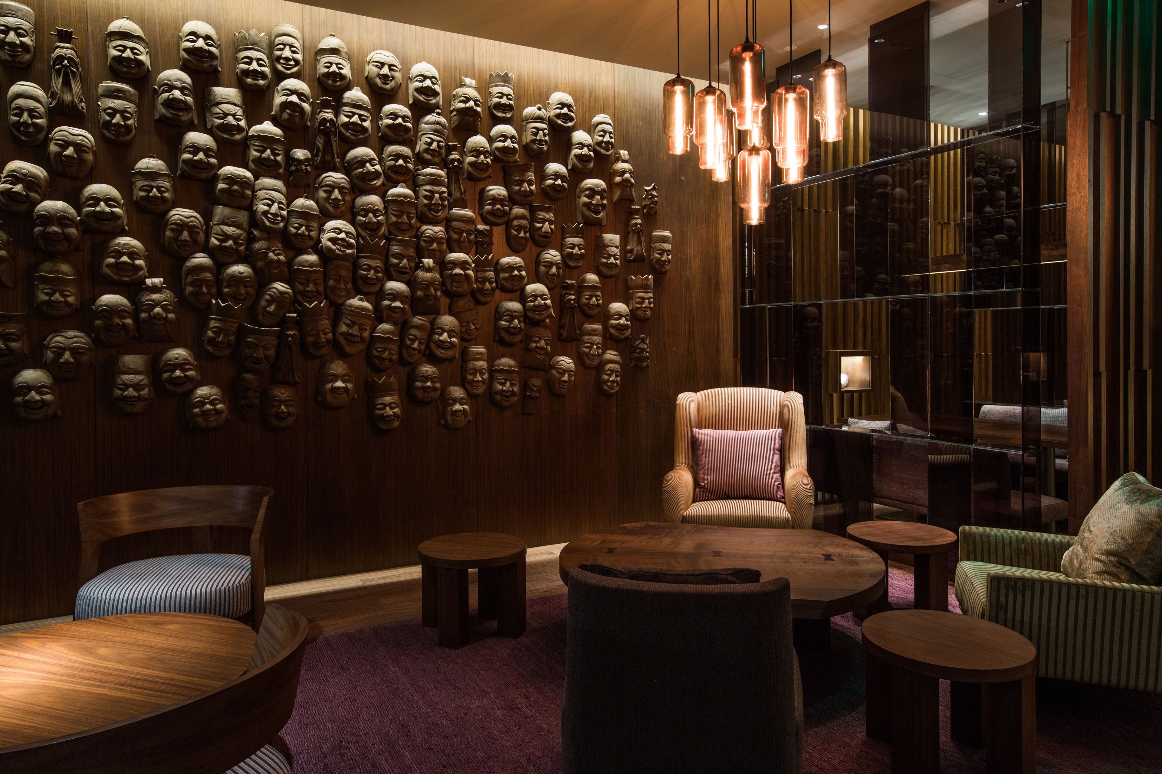 A room with a wall of carved masks, wooden furniture, and hanging pendant lights.
