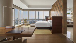 Una habitación de hotel moderna con una cama grande, un escritorio y vistas a un paisaje urbano.