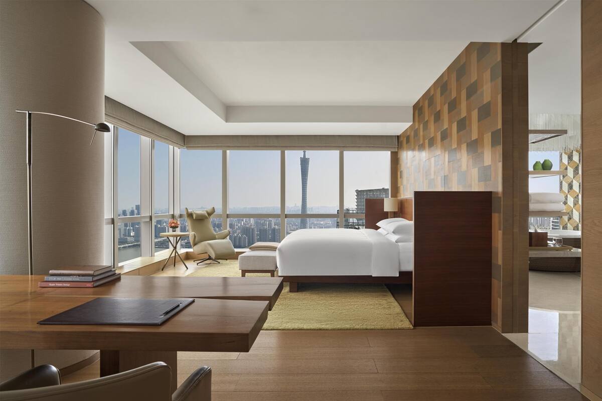 Una habitación de hotel moderna con una cama grande, un escritorio y vistas a un paisaje urbano.