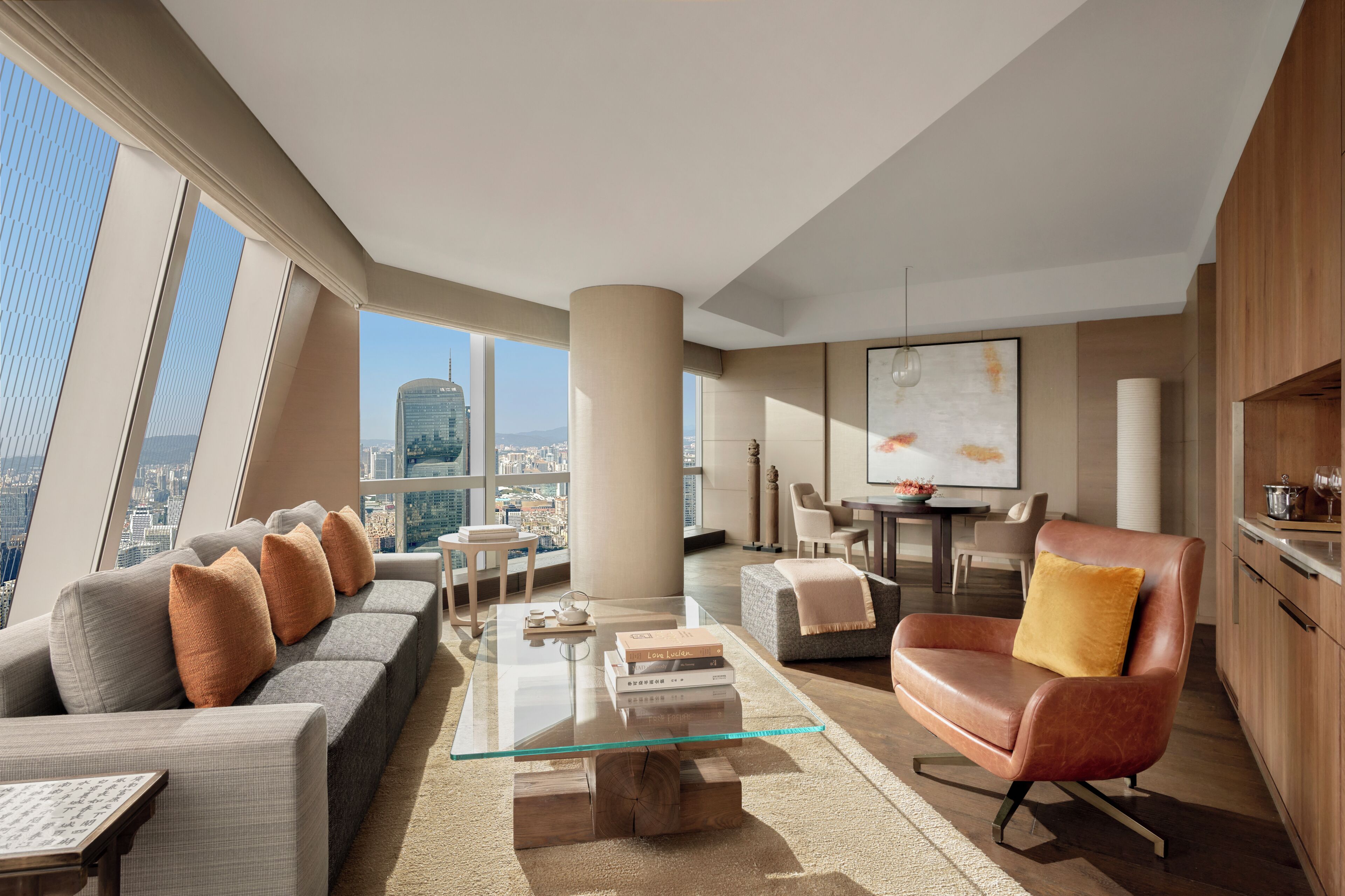 A modern living room with a glass coffee table, sofas, a leather armchair, and a city view.