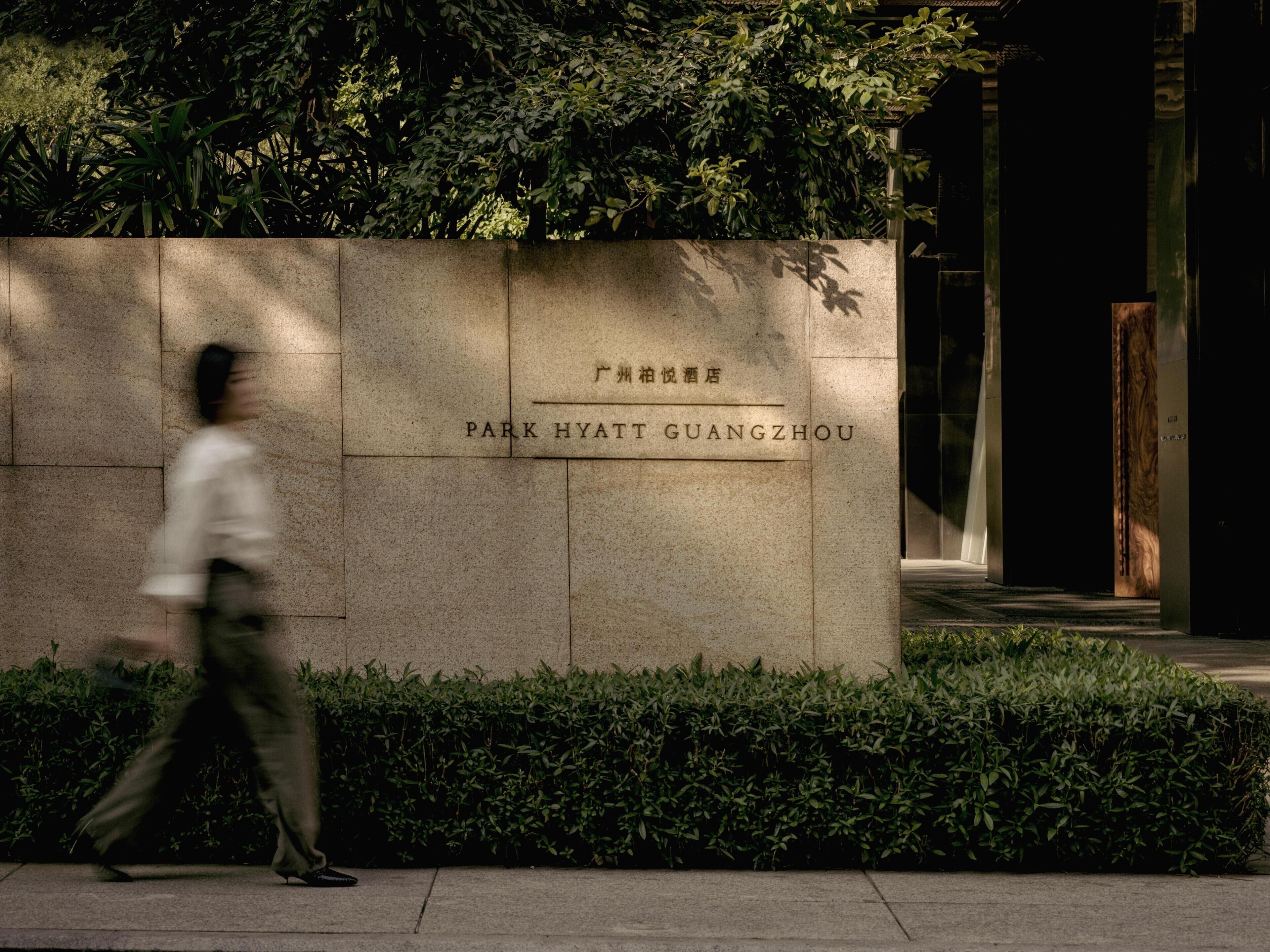 En stenvæg med 'Park Hyatt Guangzhou' indgraveret, omgivet af grøn bevoksning.