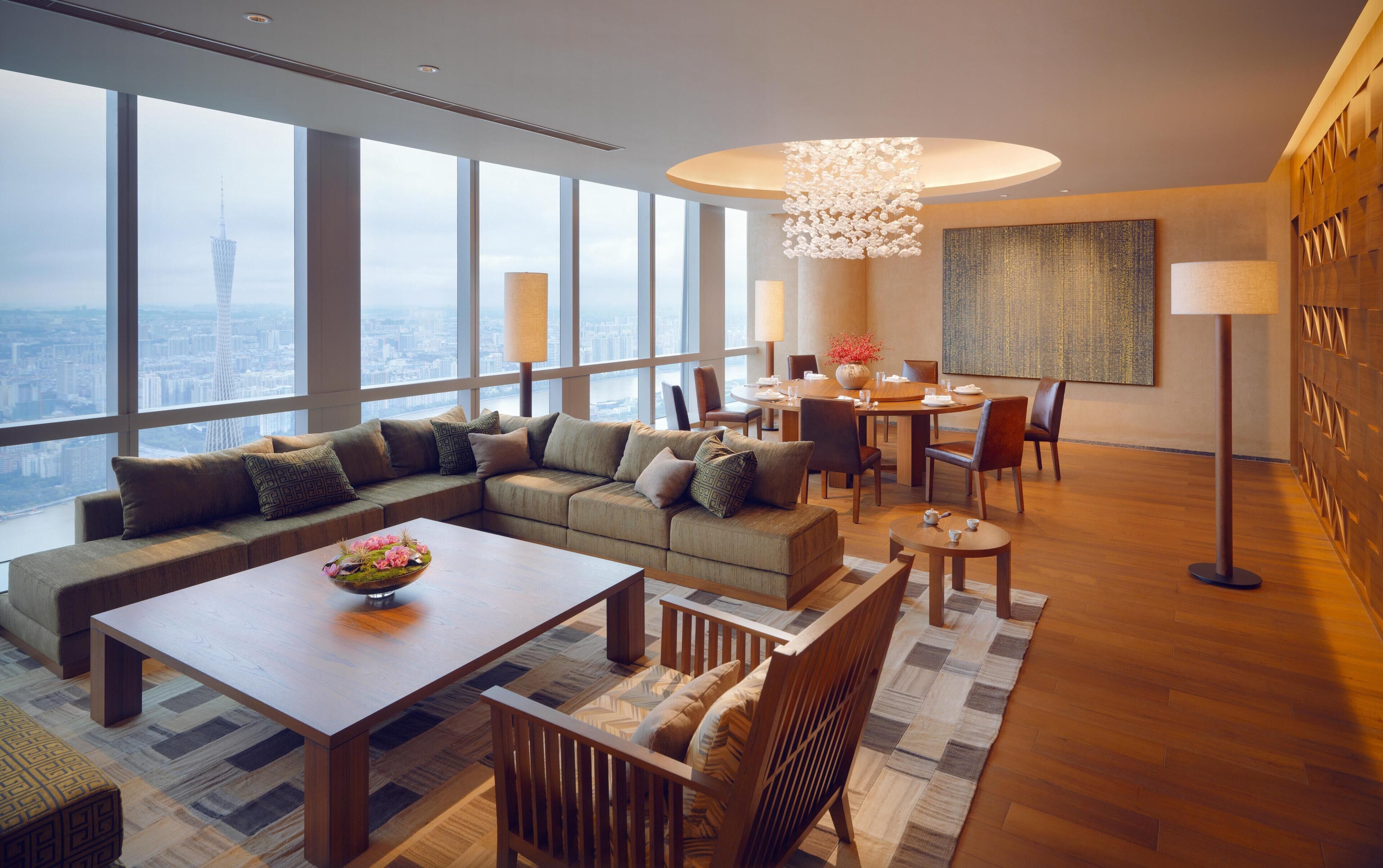 A modern living room with a sectional sofa, a dining area, and a large window offering a city view.