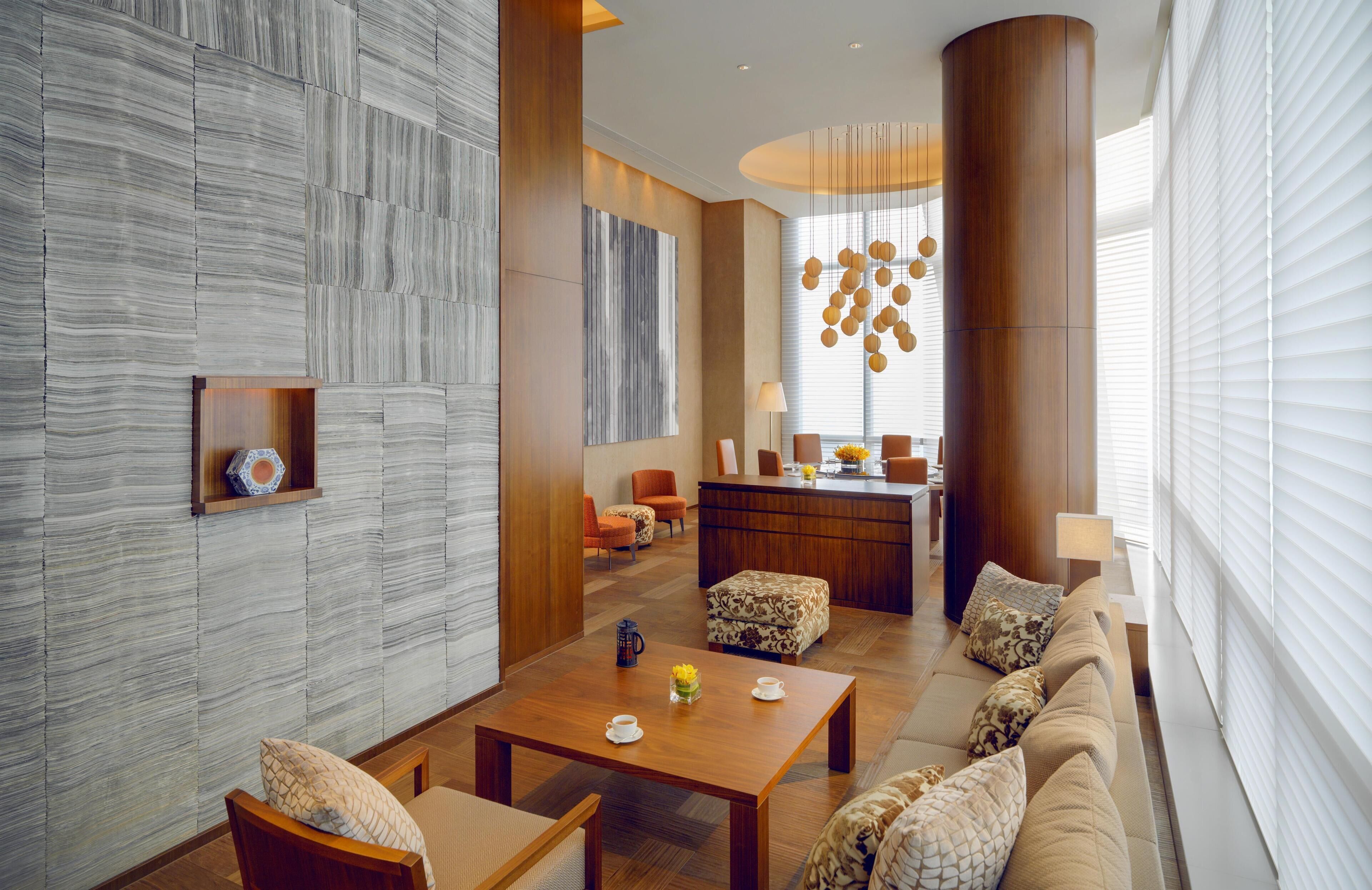 Een modern interieur met een houten salontafel, een bank en stoelen, een keukenhoek en een groot raam met zonwering.