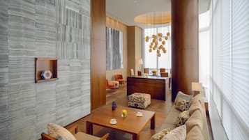 Un intérieur moderne avec une table basse en bois, un canapé et des fauteuils, un coin cuisine et une grande fenêtre équipée de stores.