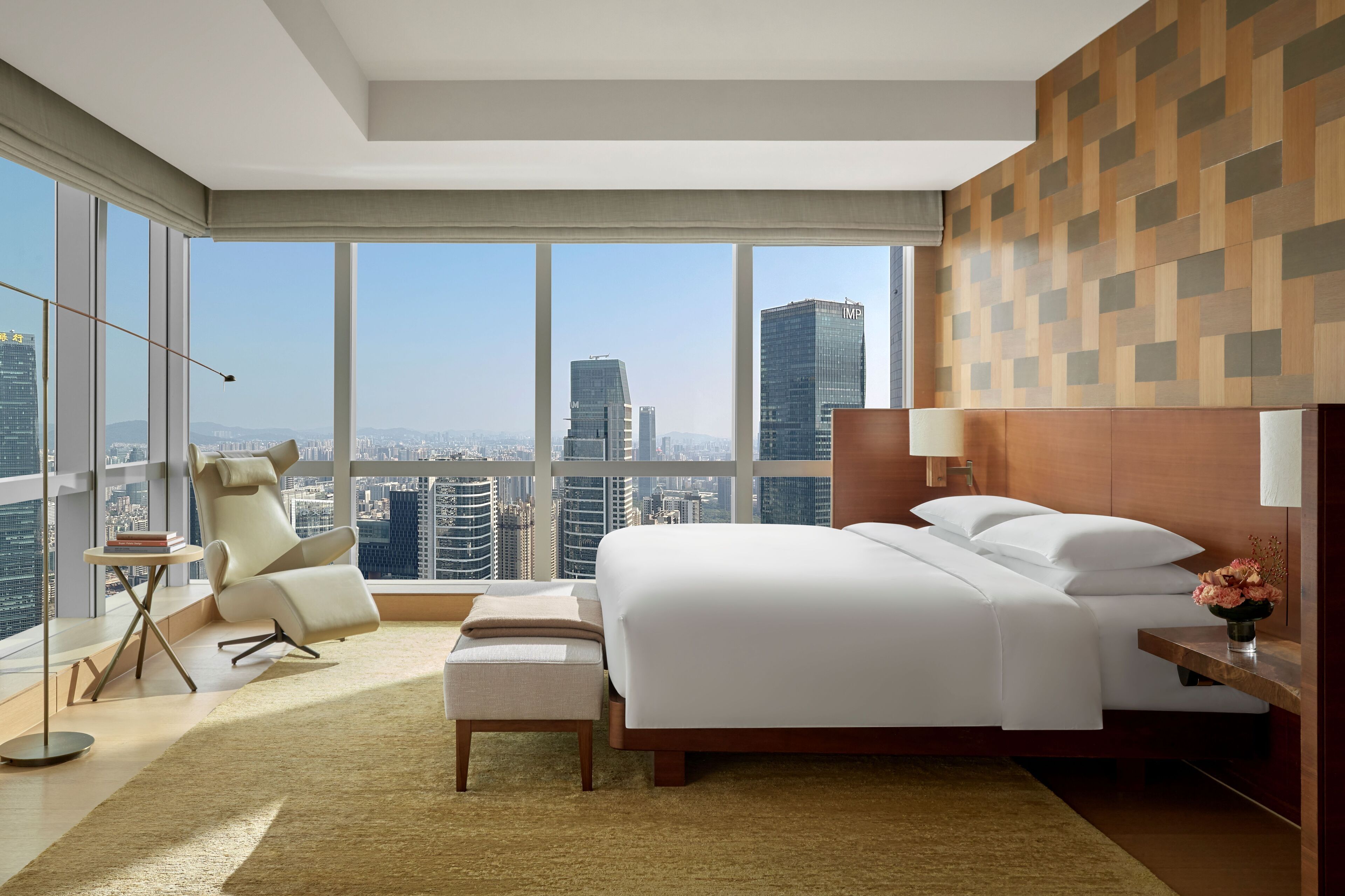 A modern hotel room with a large bed, a sitting area, and a view of the cityscape.